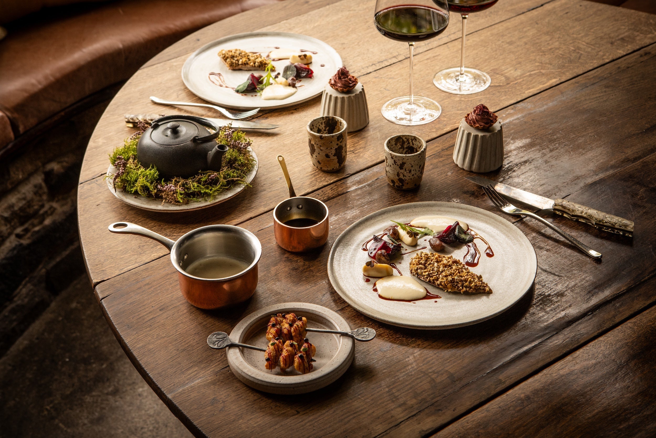 Chef in wellies at rustic table with minimalist gourmet plates, copper cookware