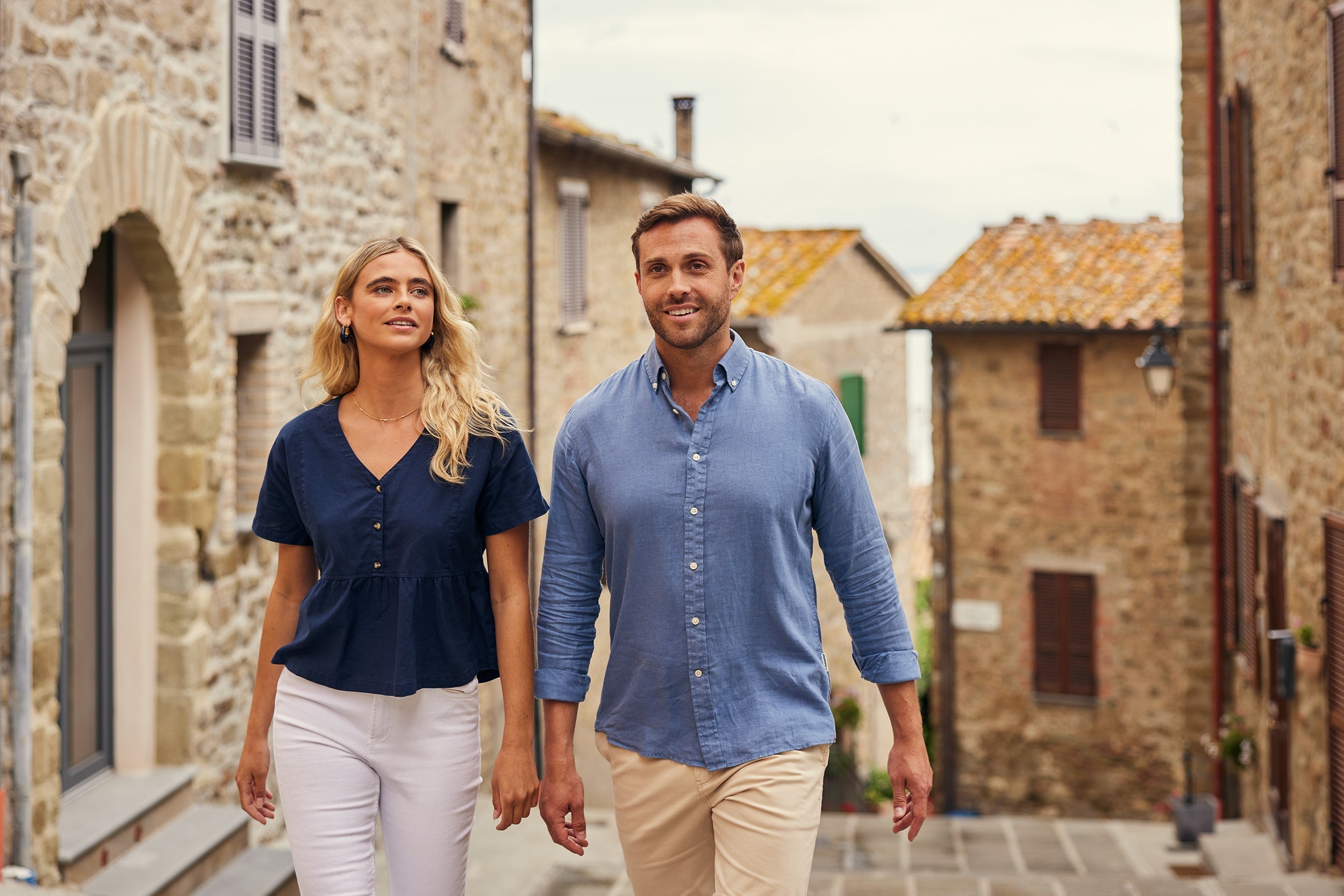 Couple in linen outfits stroll hand-in-hand on cobblestone alley