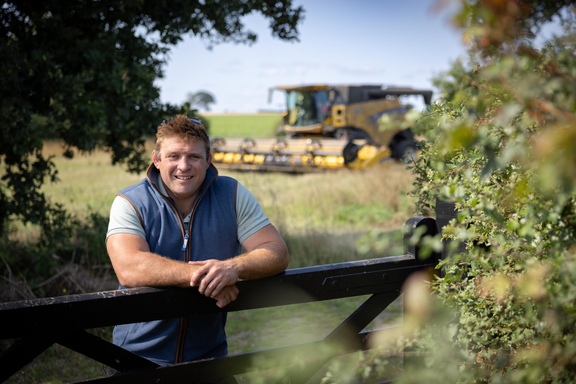 Rugby legend Tom Youngs in blue vest leaning on black gate at harvest time