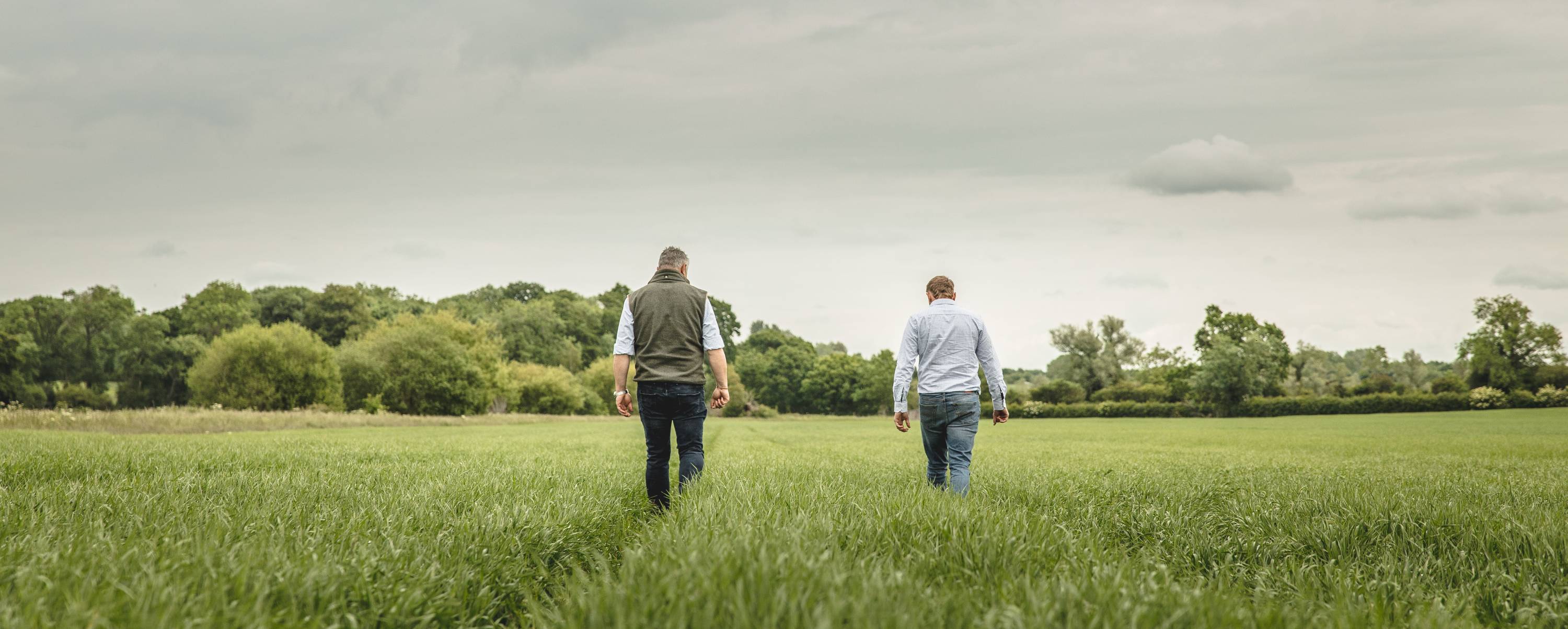 Two farmers walking green field under overcast sky amid budget unrest