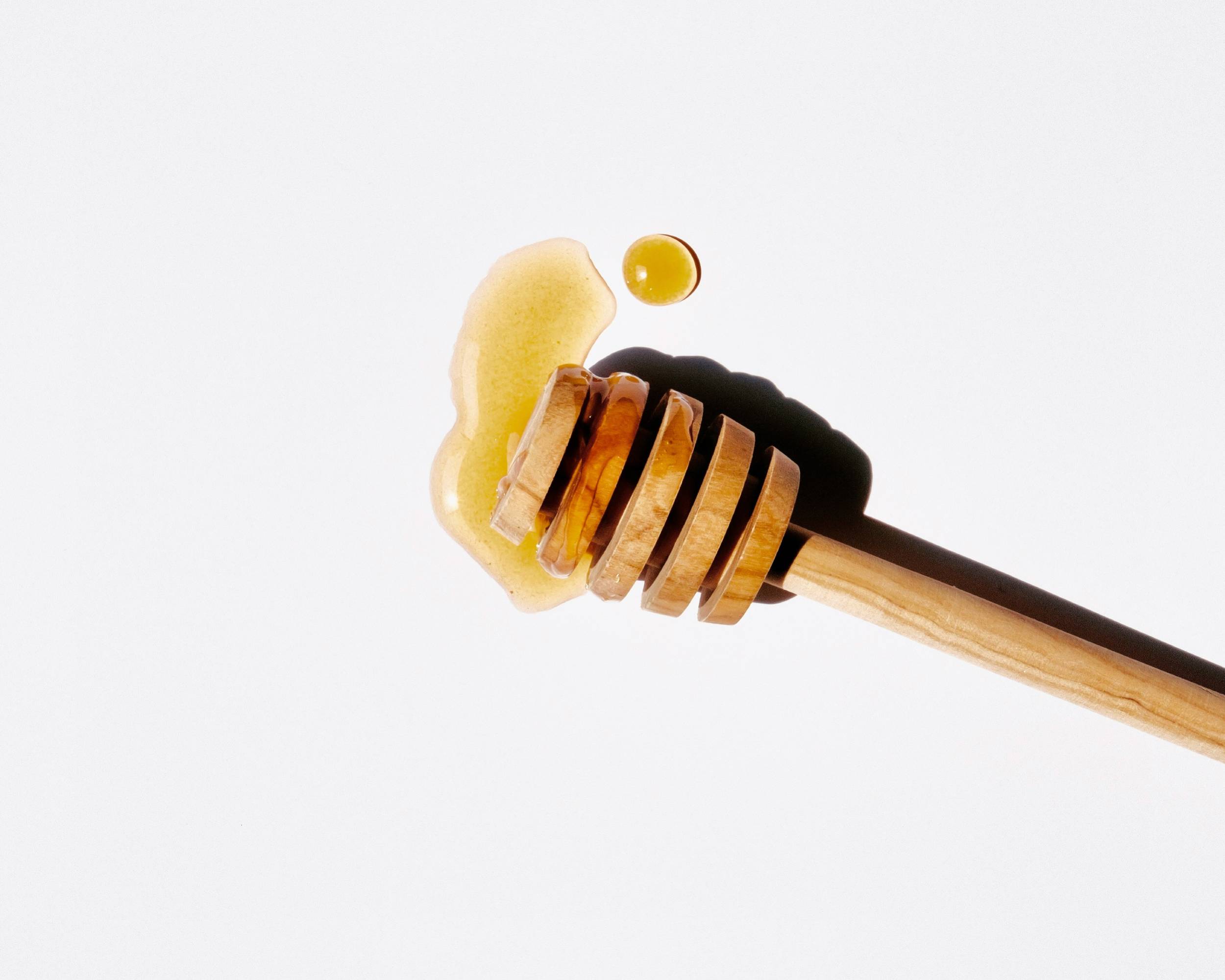 Wooden honey dipper dripping golden amber honey in fraud article