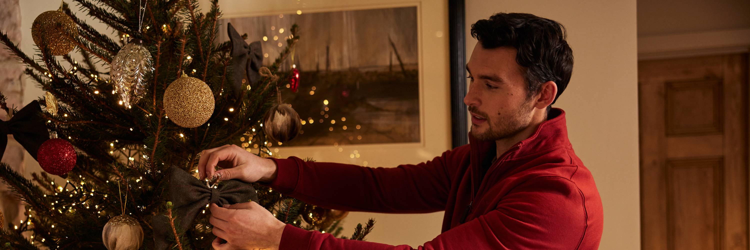 Man in red velvet jacket decorating Christmas tree with gold silver ornaments