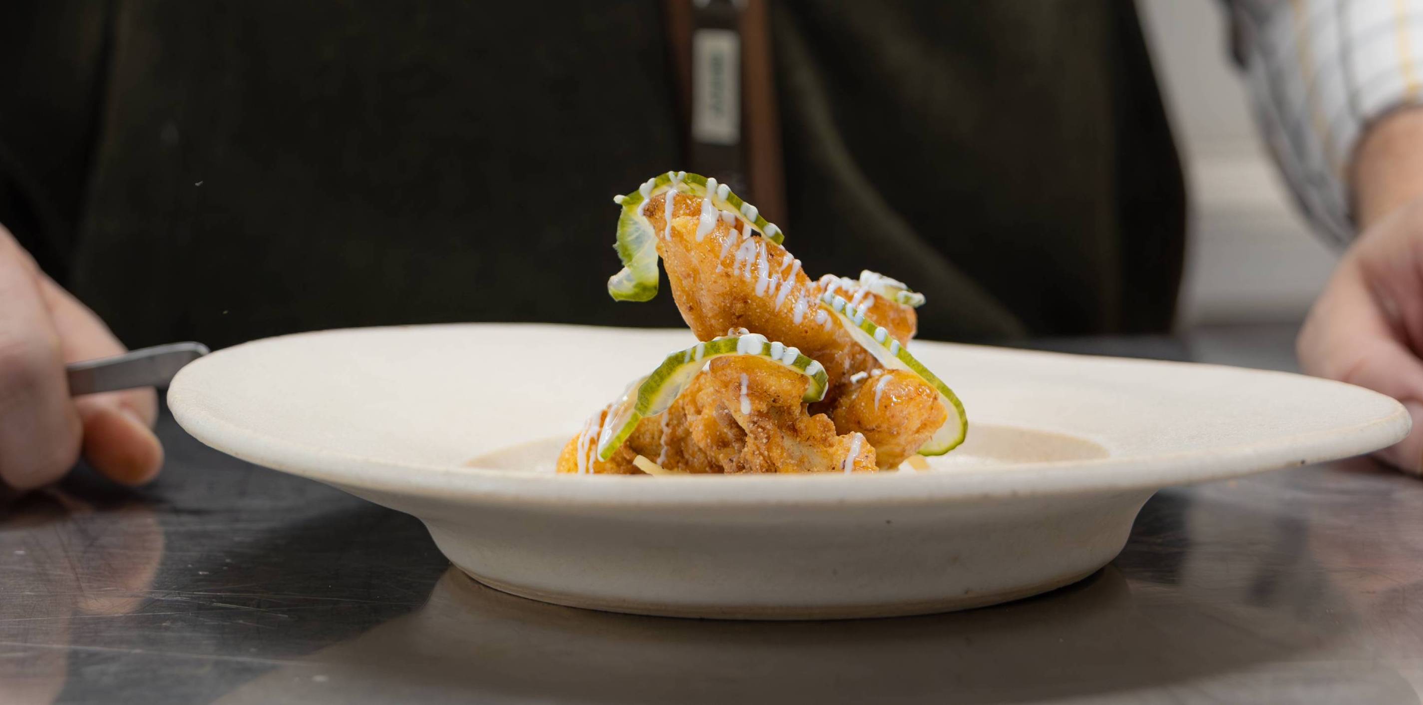 Golden-brown fried chicken wing garnished with green ribbons and white sauce drizzle
