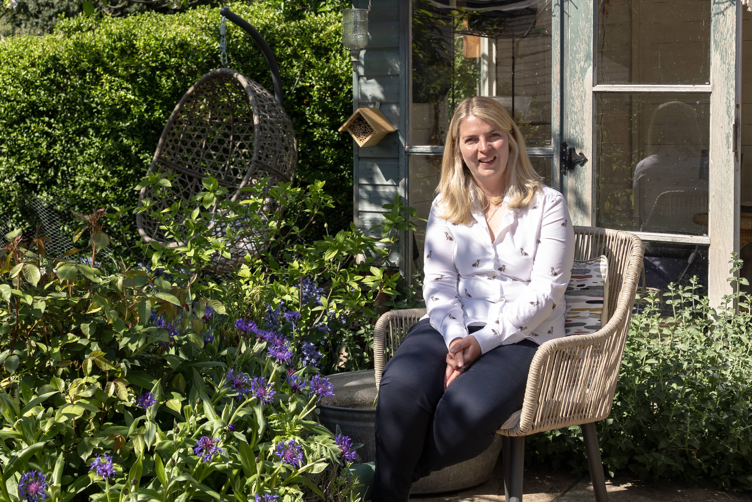 Woman in white blouse with black insect print on wicker chair for RHS Chelsea Flower Show garden design with Nicola Oakey