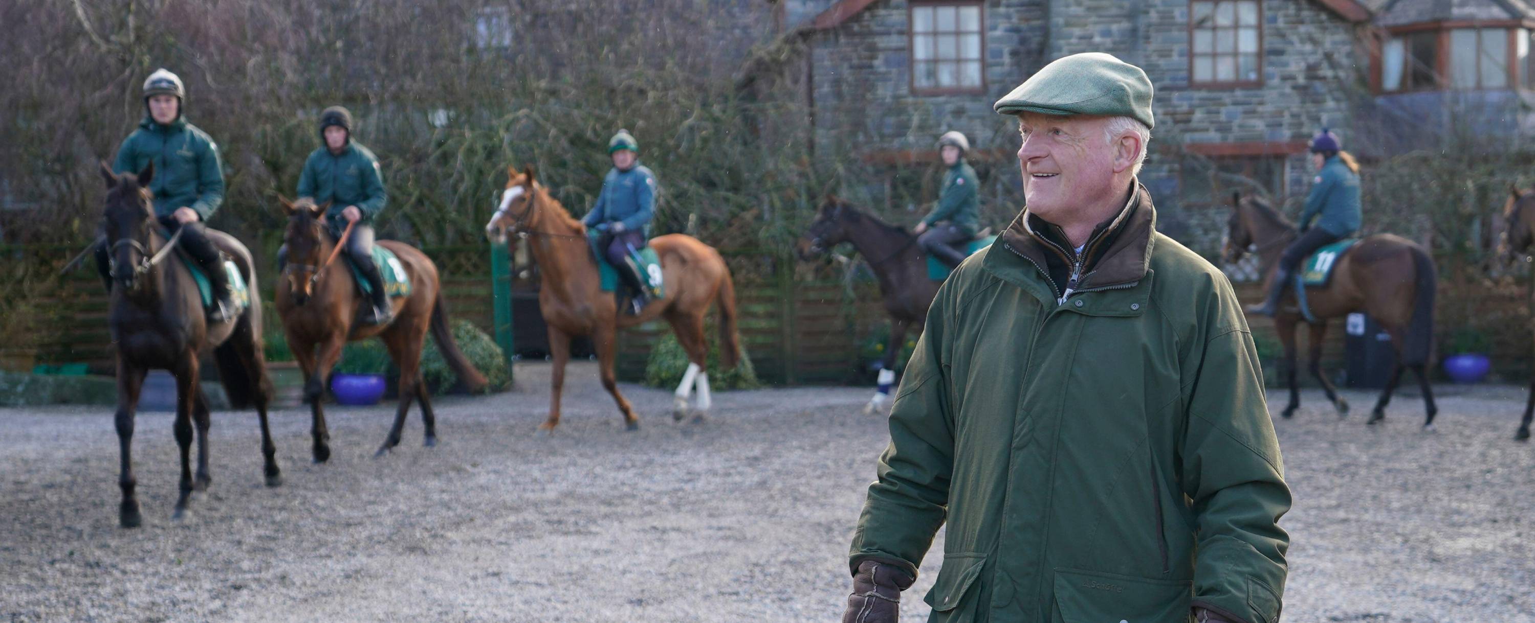 Willie Mullins in green tweed cap smiling with horse riders behind, Cotswolds
