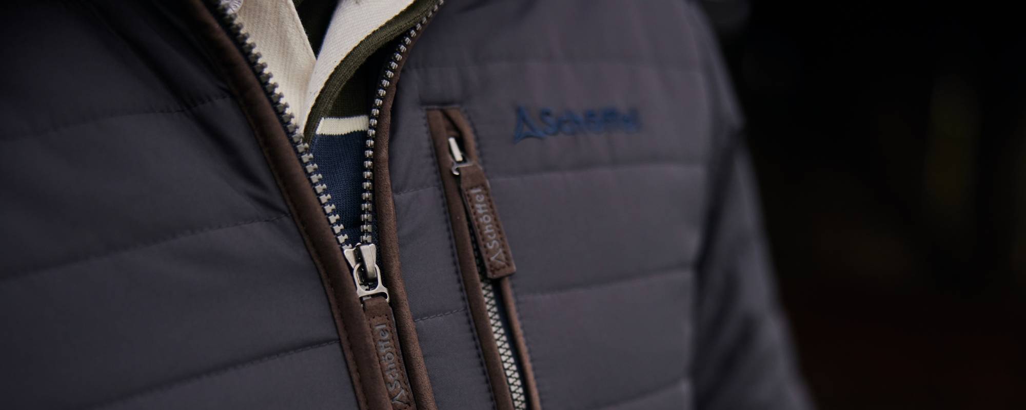 Dark gray quilted PrimaLoft jacket with brown zippers and blue logo