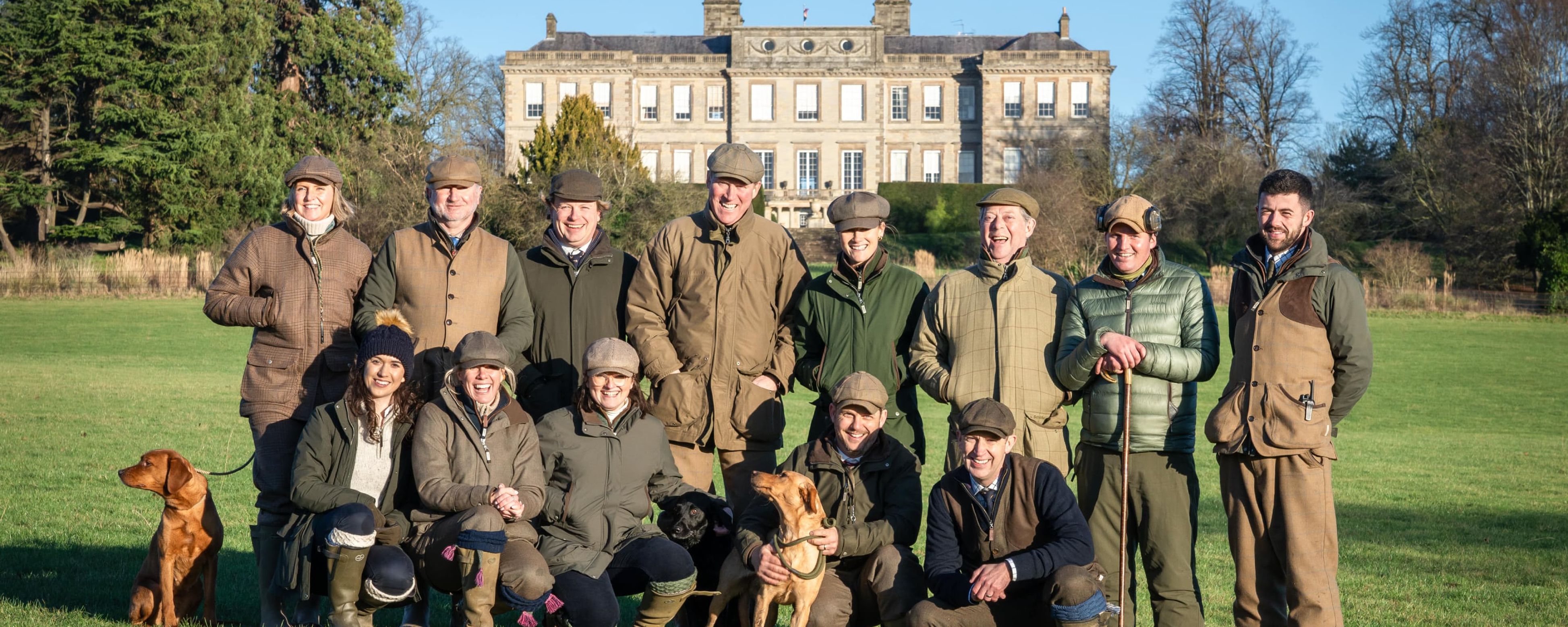 Schoffel Country team in earth-toned attire posing with dogs before stone manor