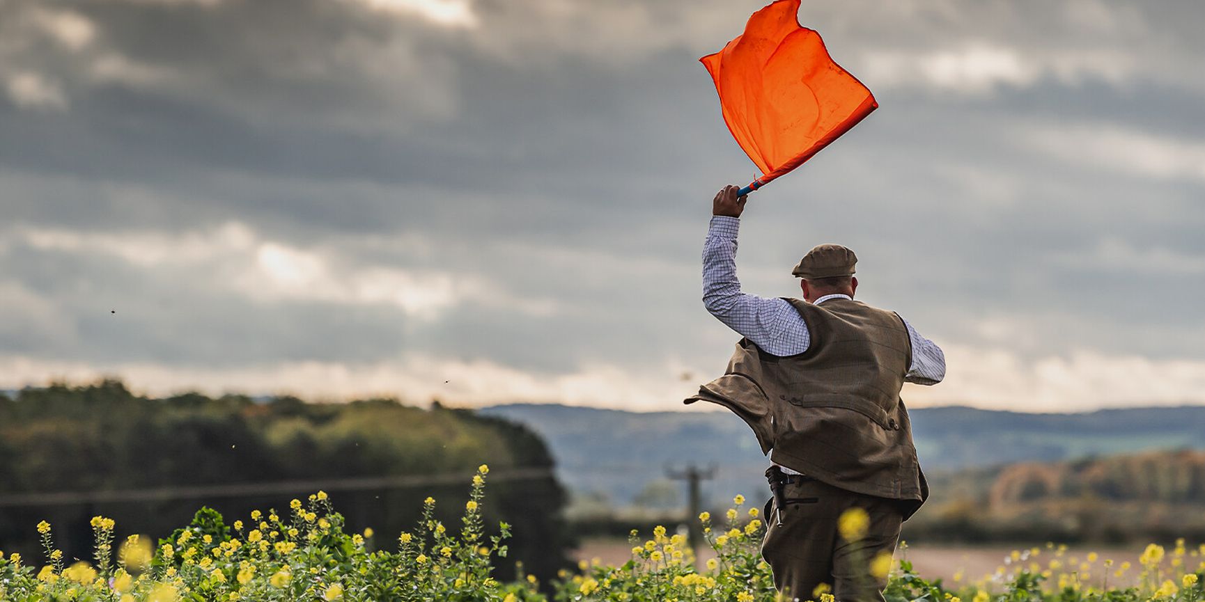 Gamekeeper waving bright orange flag in autumn field