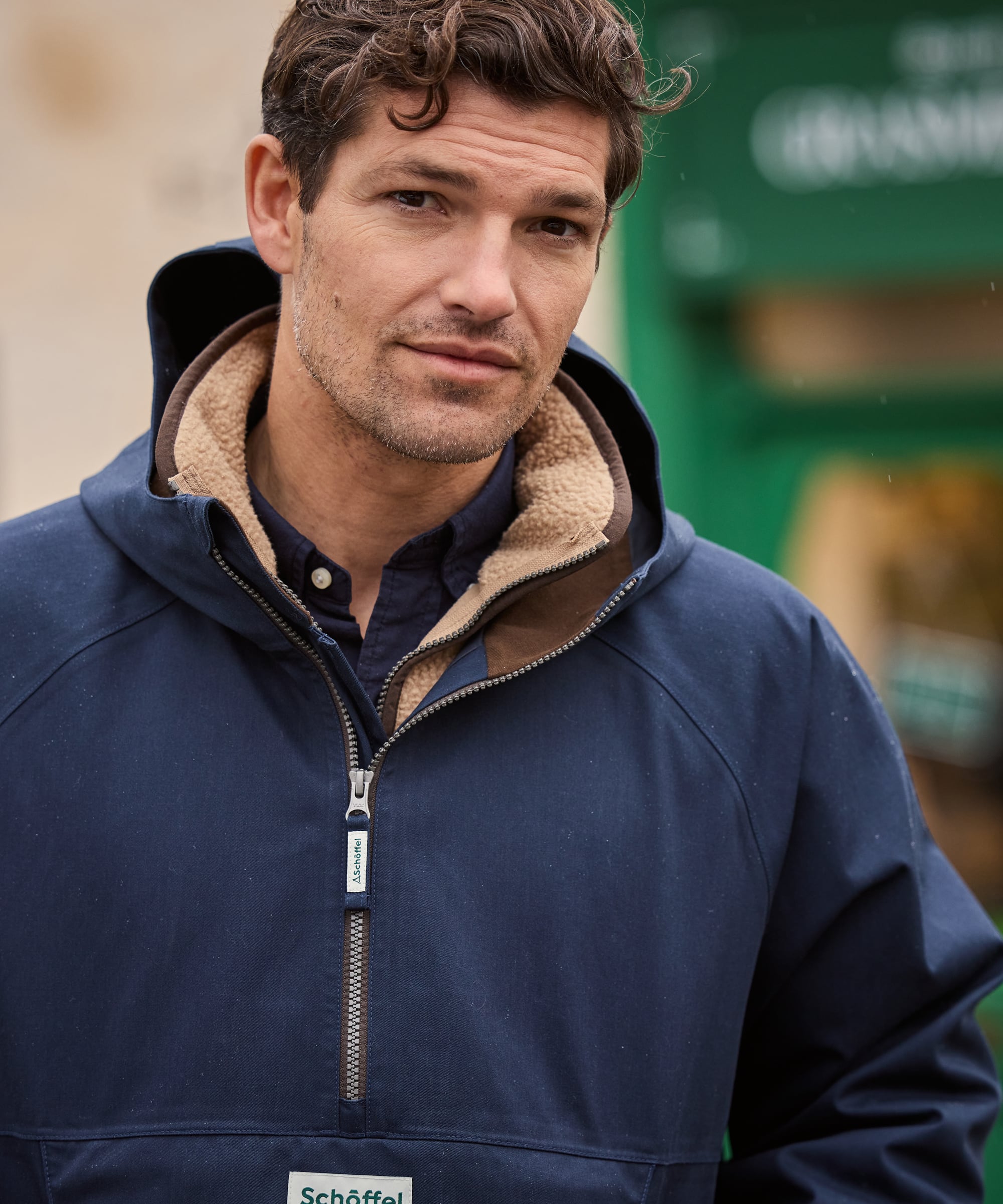 Man wearing a blue jacket with a brand logo, standing outdoors.