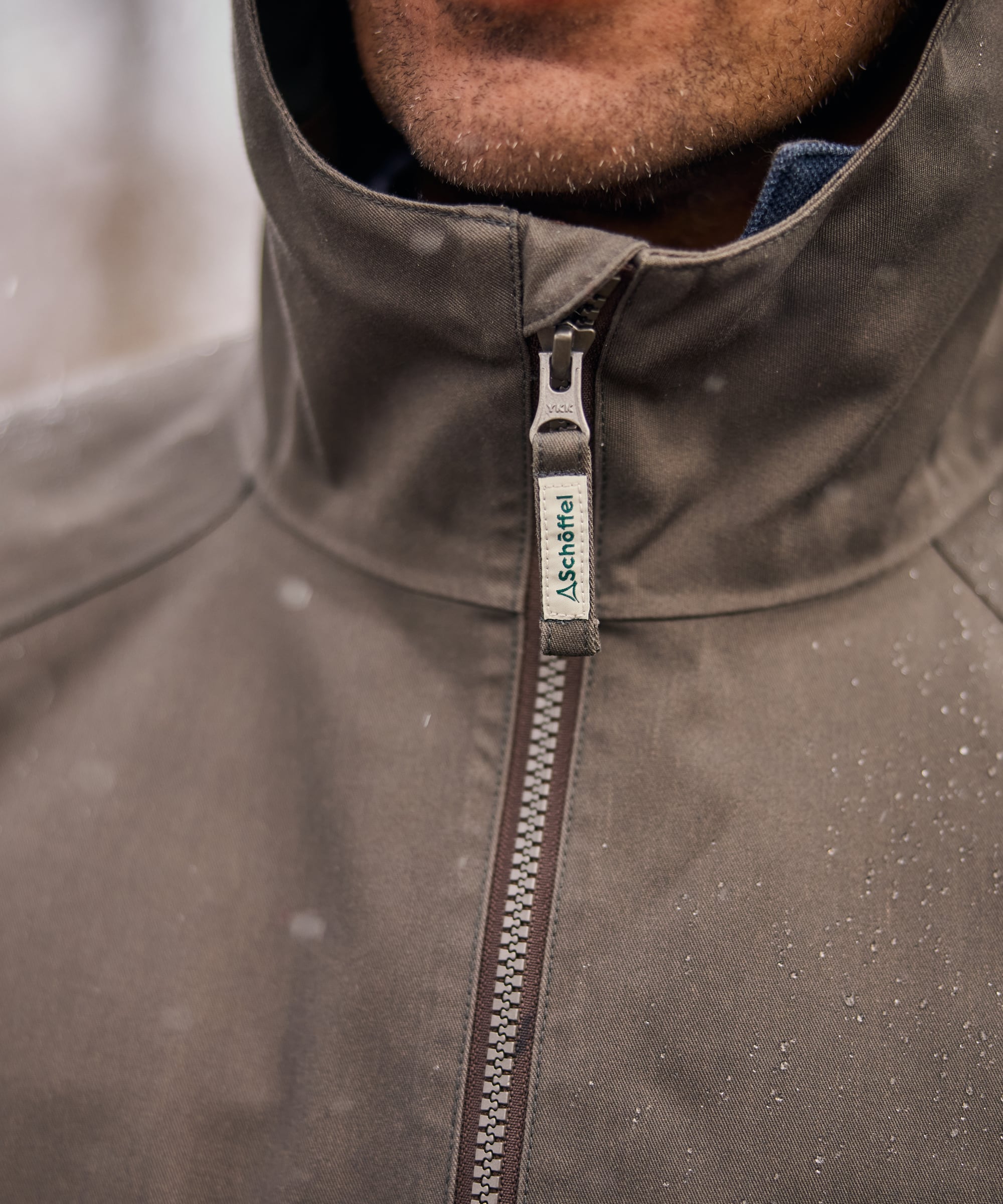 Close-up of a green jacket with a zipper and brand label, blurred background