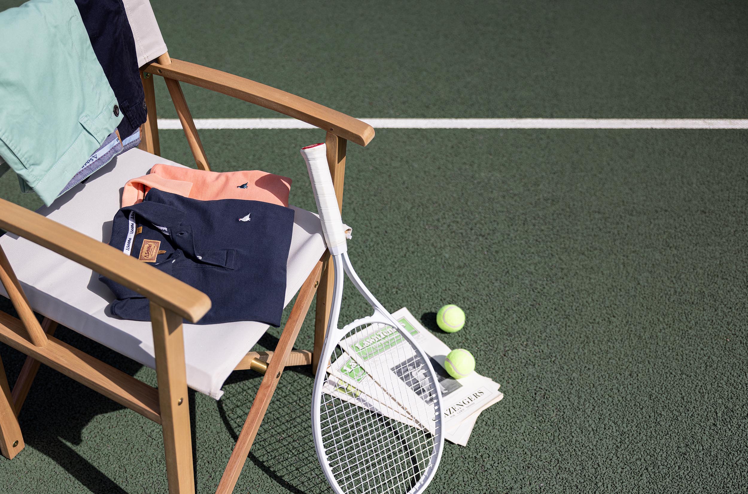 Tennis racket and balls on a tennis court with a chair and clothing items.