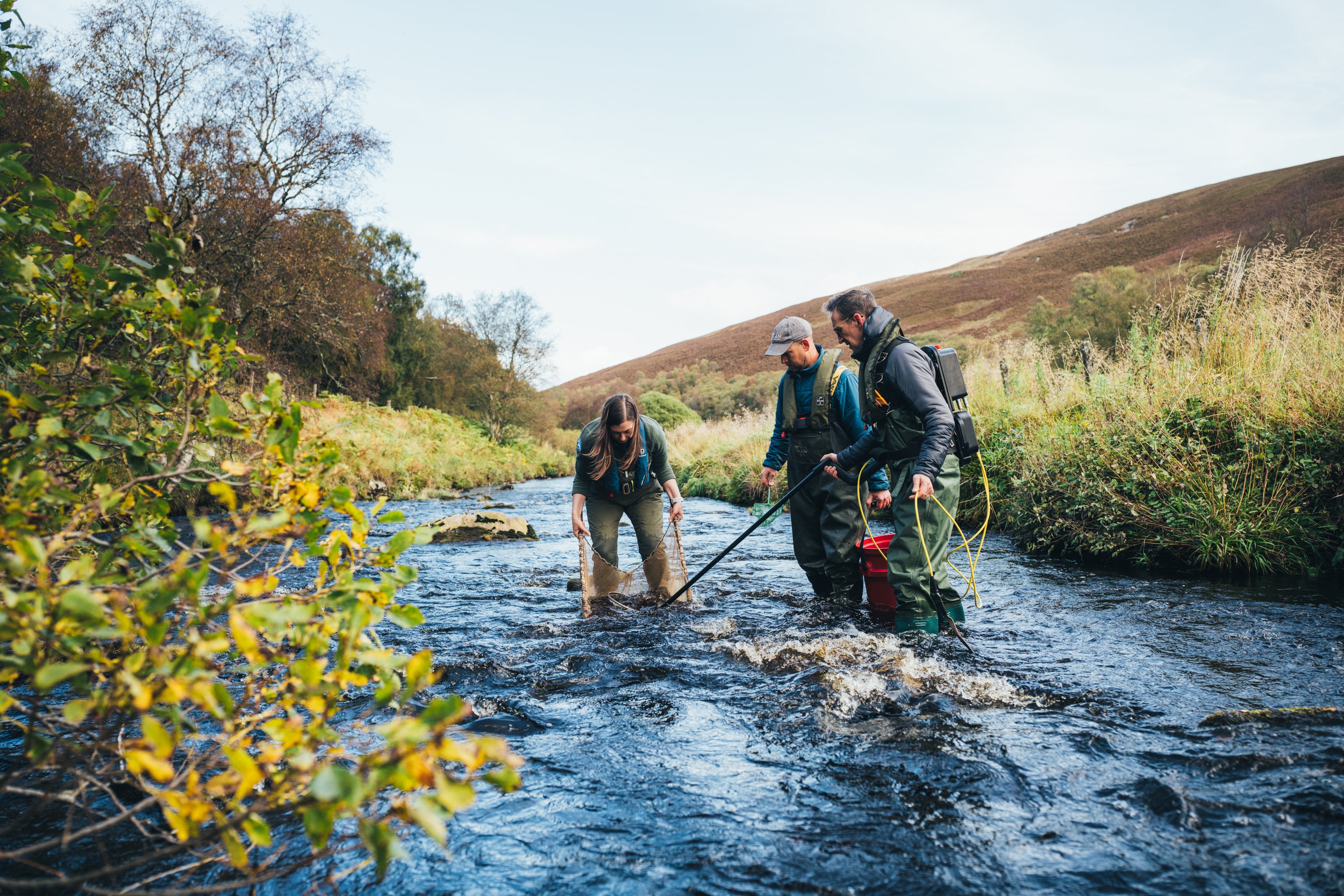 A group of people standing in a river, looking down.