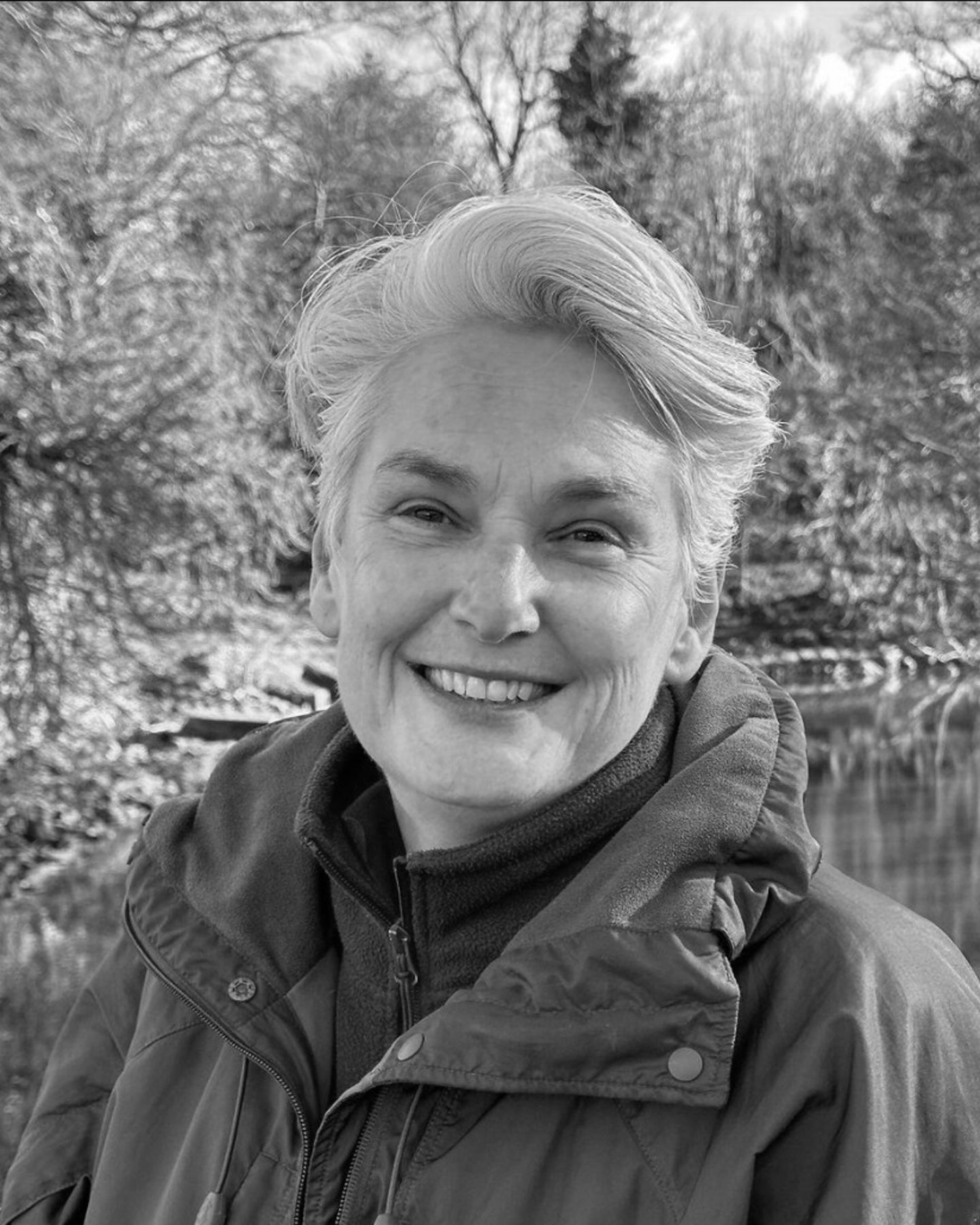 Black and white photo of Alison Baker in the outdoors with trees and a pond in the background