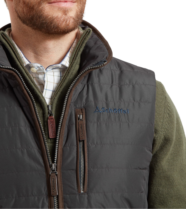 Close-up of a man wearing a charcoal quilted gilet with brown suede-effect zip trims and a navy