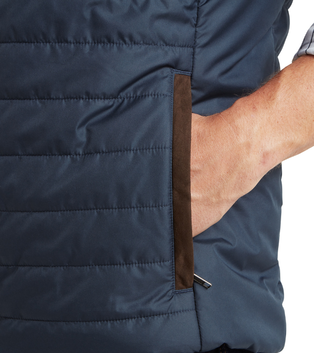 Close-up detail of a navy quilted gilet showing a hand-warmer pocket with a brown suede-effect