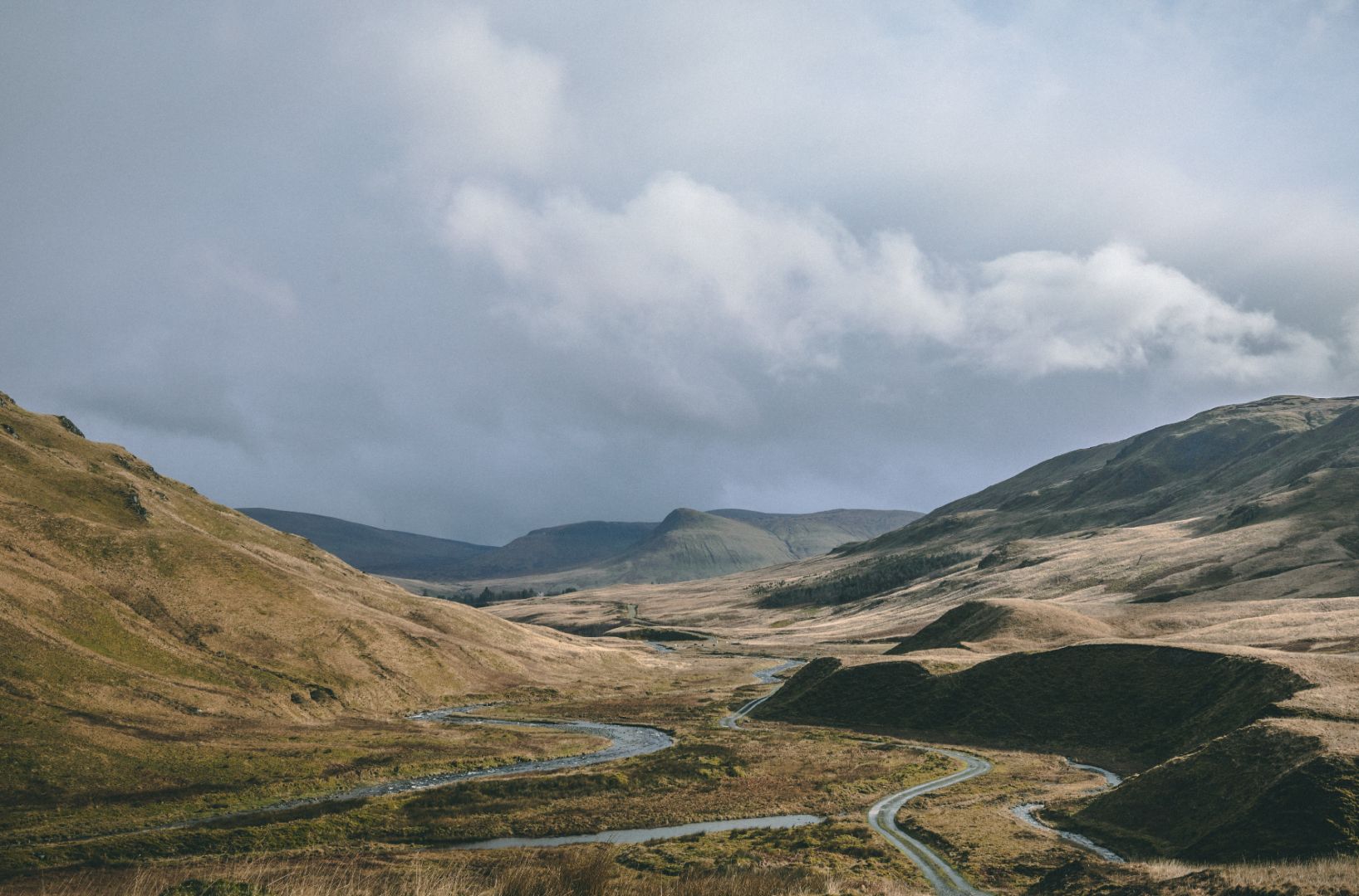 Winding road through a hilly landscape with a cloudy sky