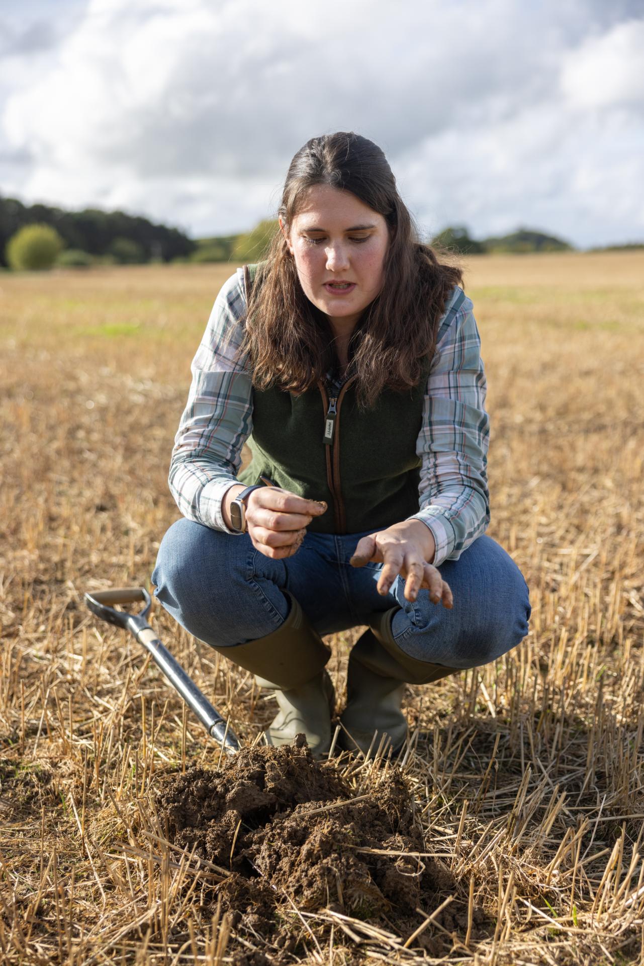 Woman examining soil in a field with tools nearby