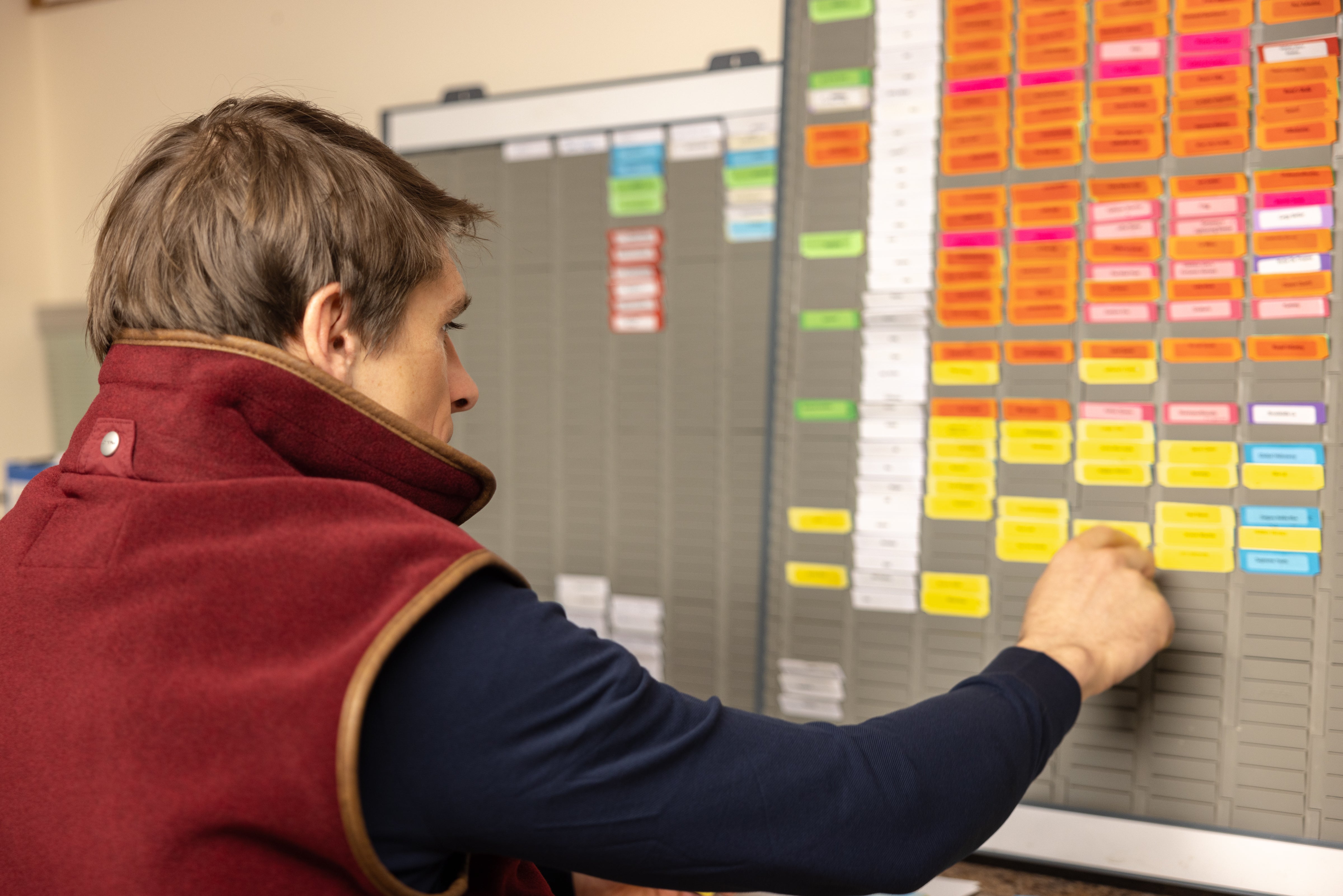 Harry Skelton, wearing a red gilet arranges a scheduling board with labels indicating the planned activities for the horses.