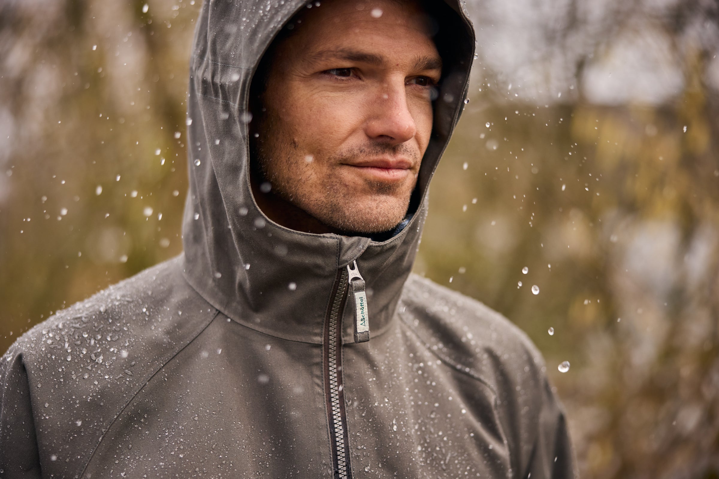 Man wearing a gray hooded jacket in a rainy forest setting