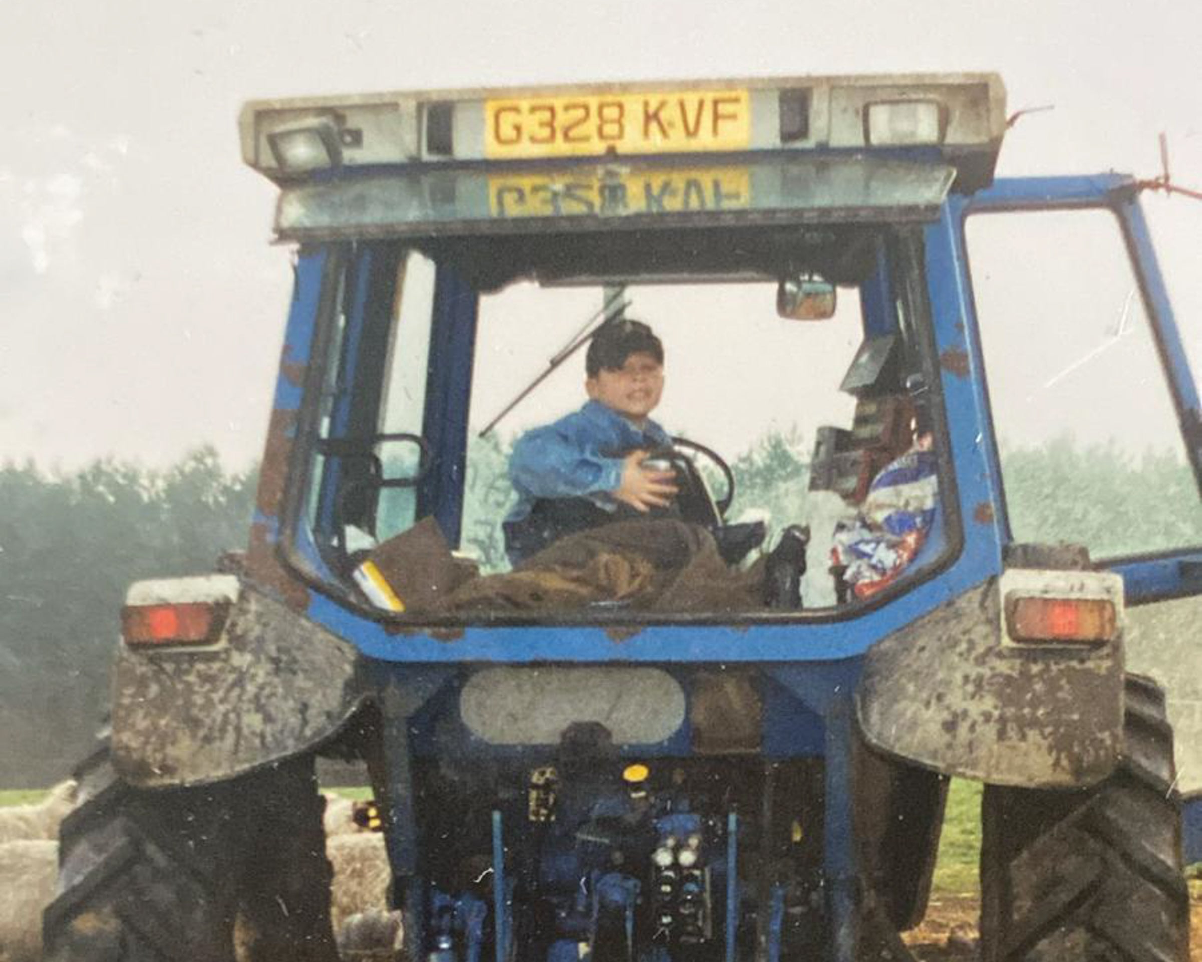 Child sitting inside a large blue tractor with visible license plate.