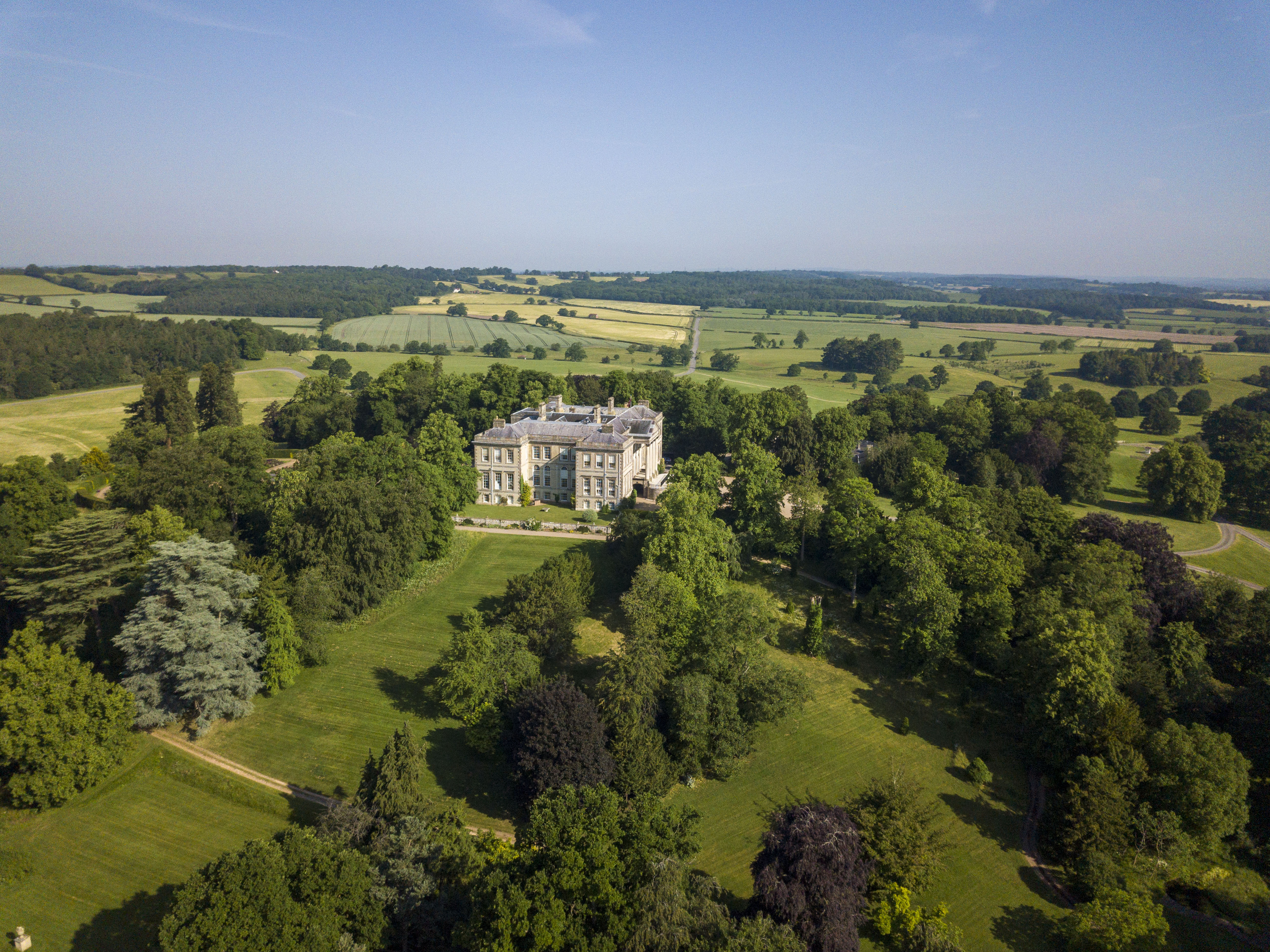 Ragley Hall surrounded by green fields and trees under a clear blue sky.