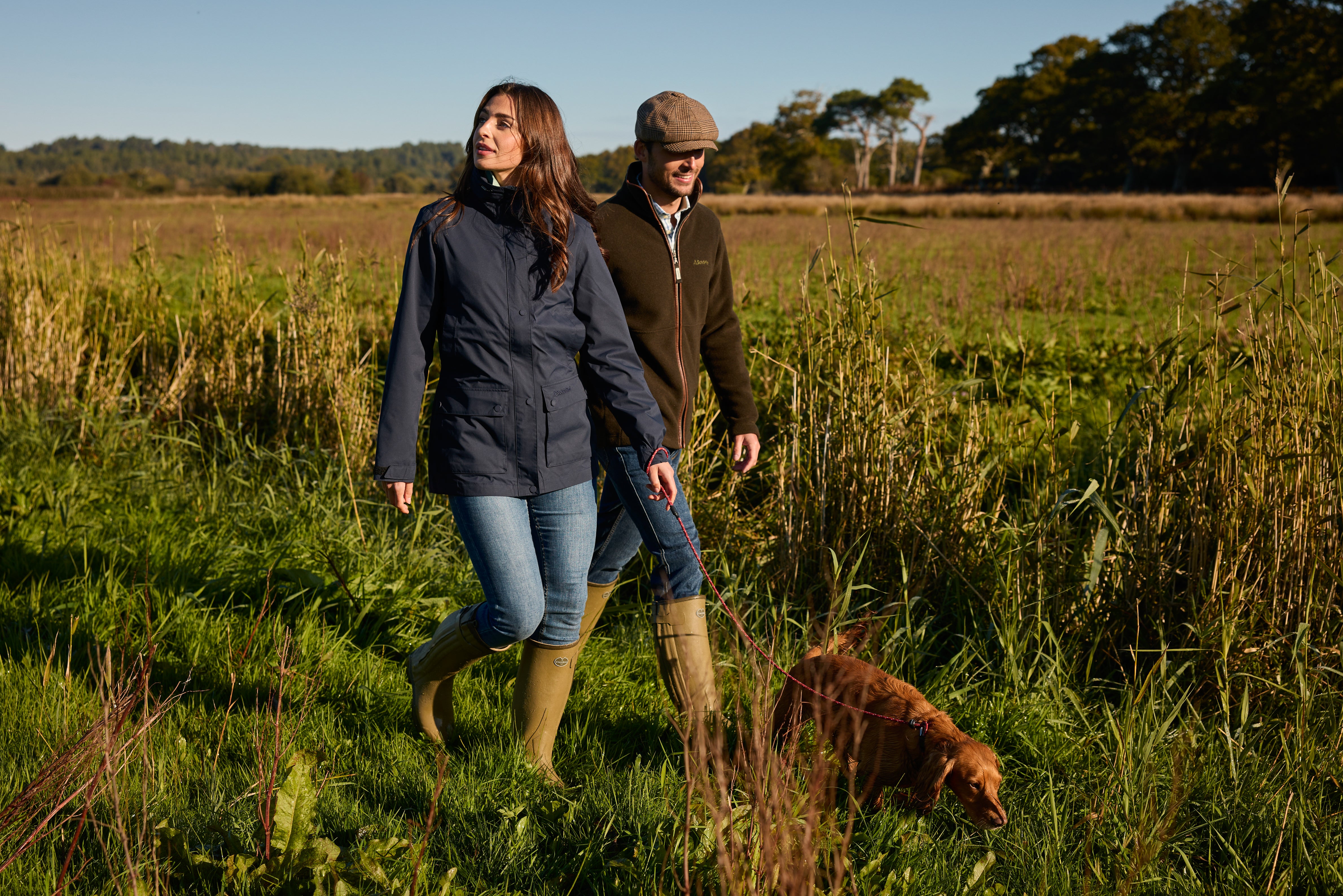 Two people walking with a dog in a field