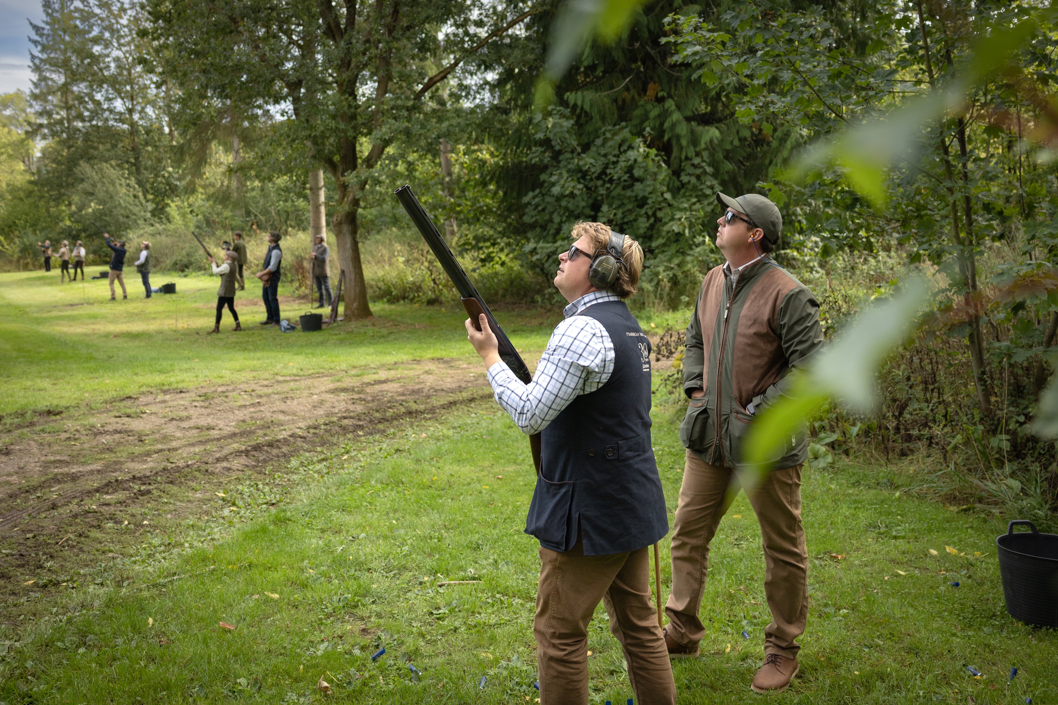 Two men in outdoor attire with one holding a shotgun in a grassy field.