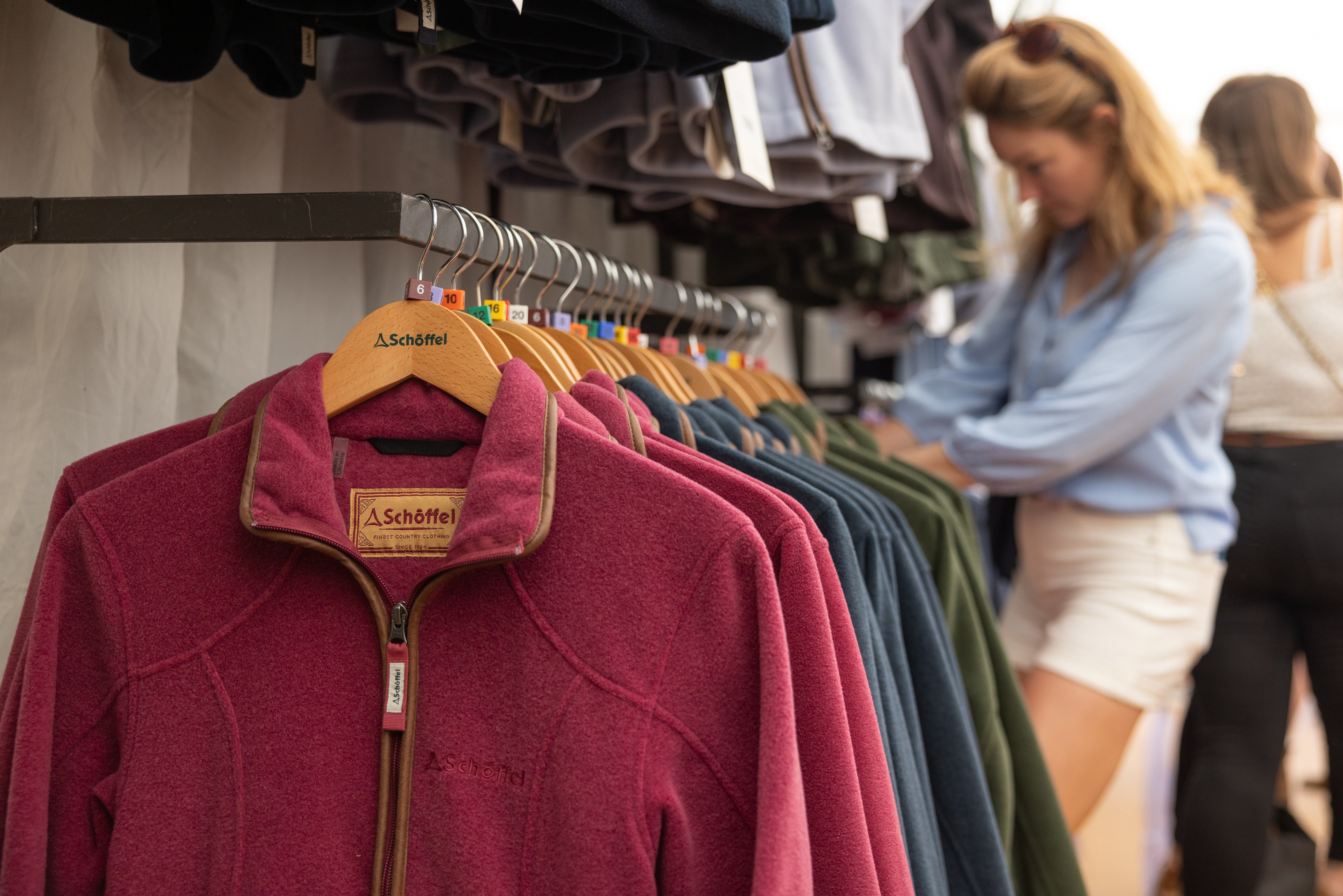 Schöffel fleece jackets on hangers with a blurred background of people shopping.