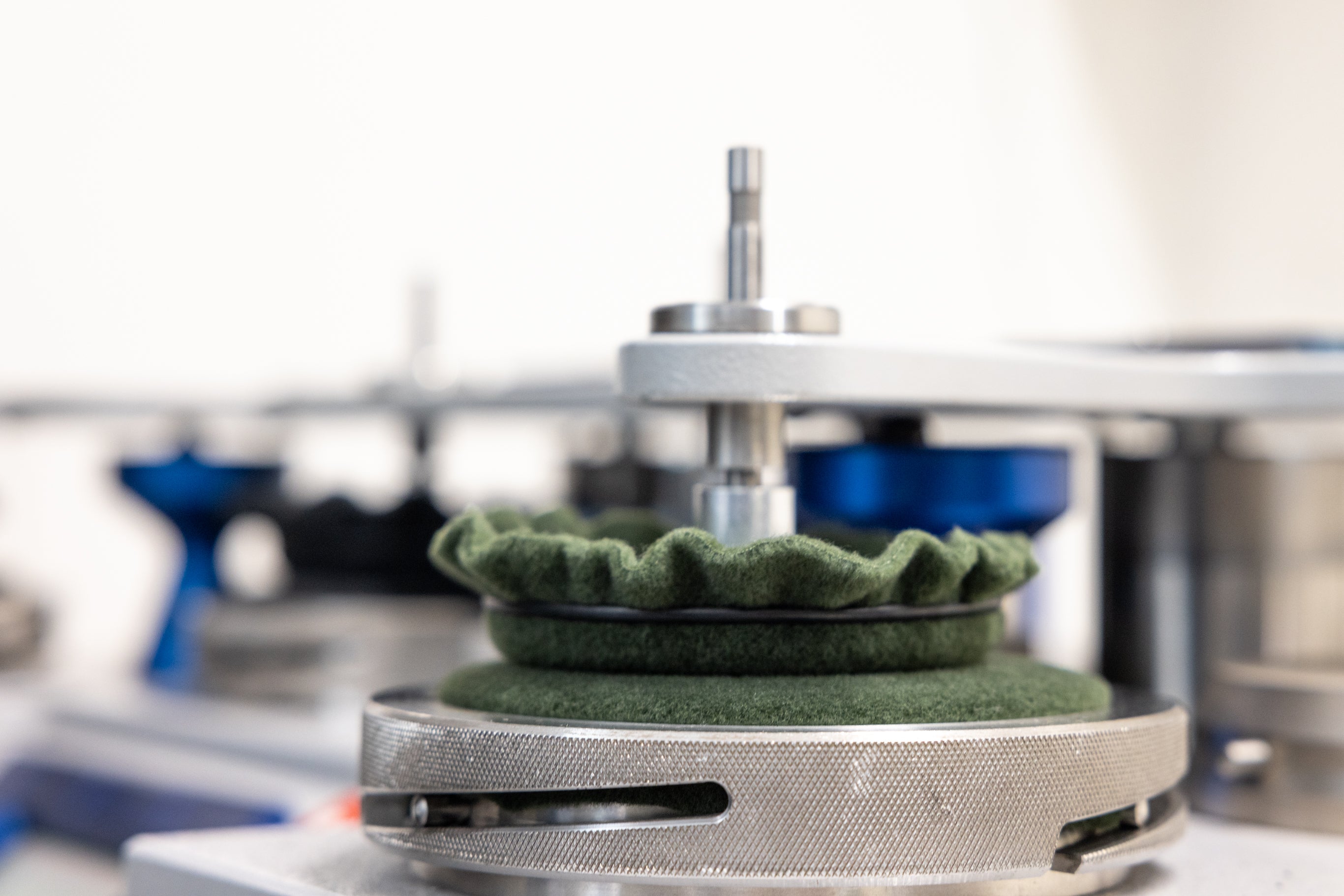 A close-up of a Schöffel green fleece mounted on a silver metal rotary press or machine component, with a blurred light grey background.
