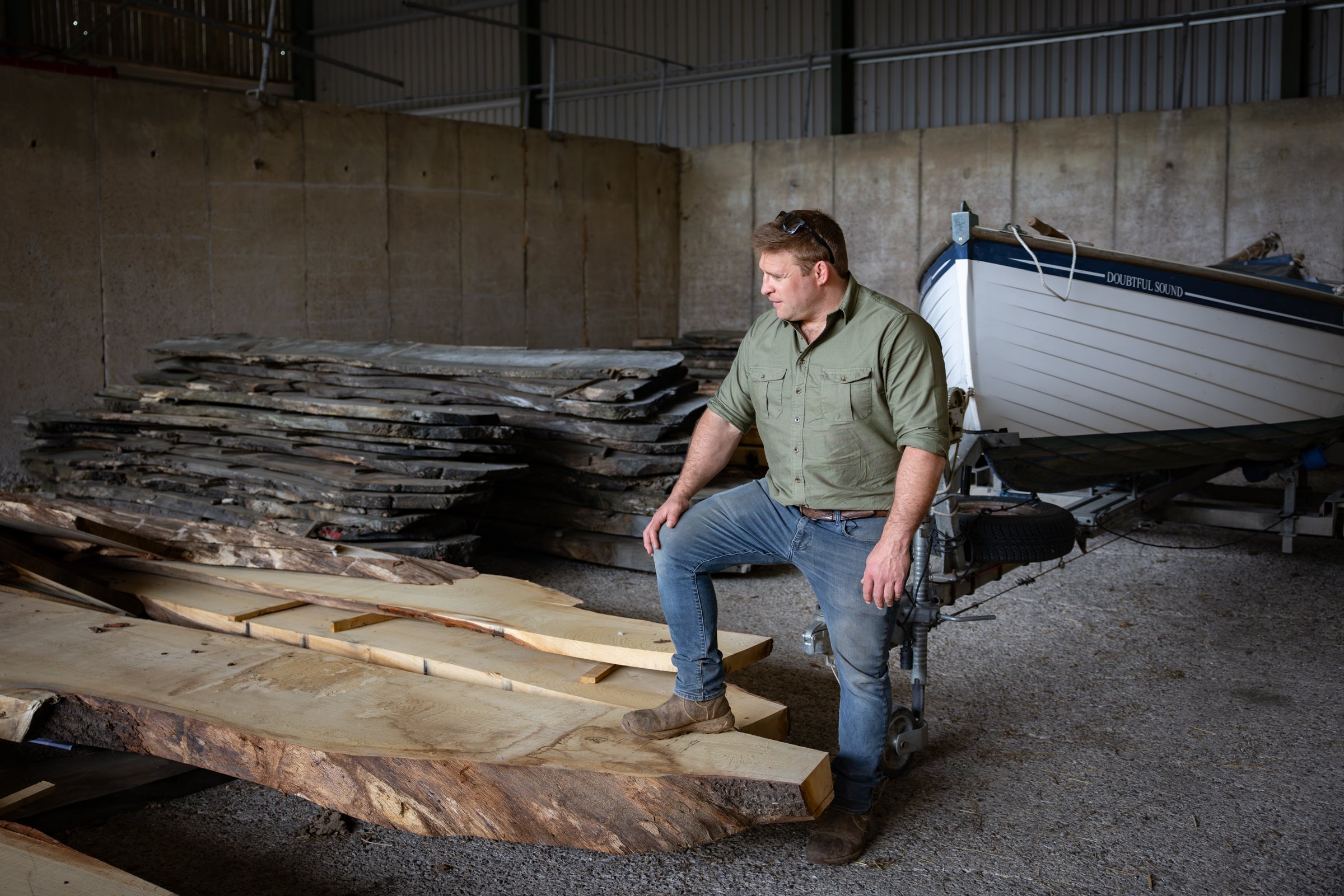 Man sitting on wooden planks in a warehouse with a boat in the background
