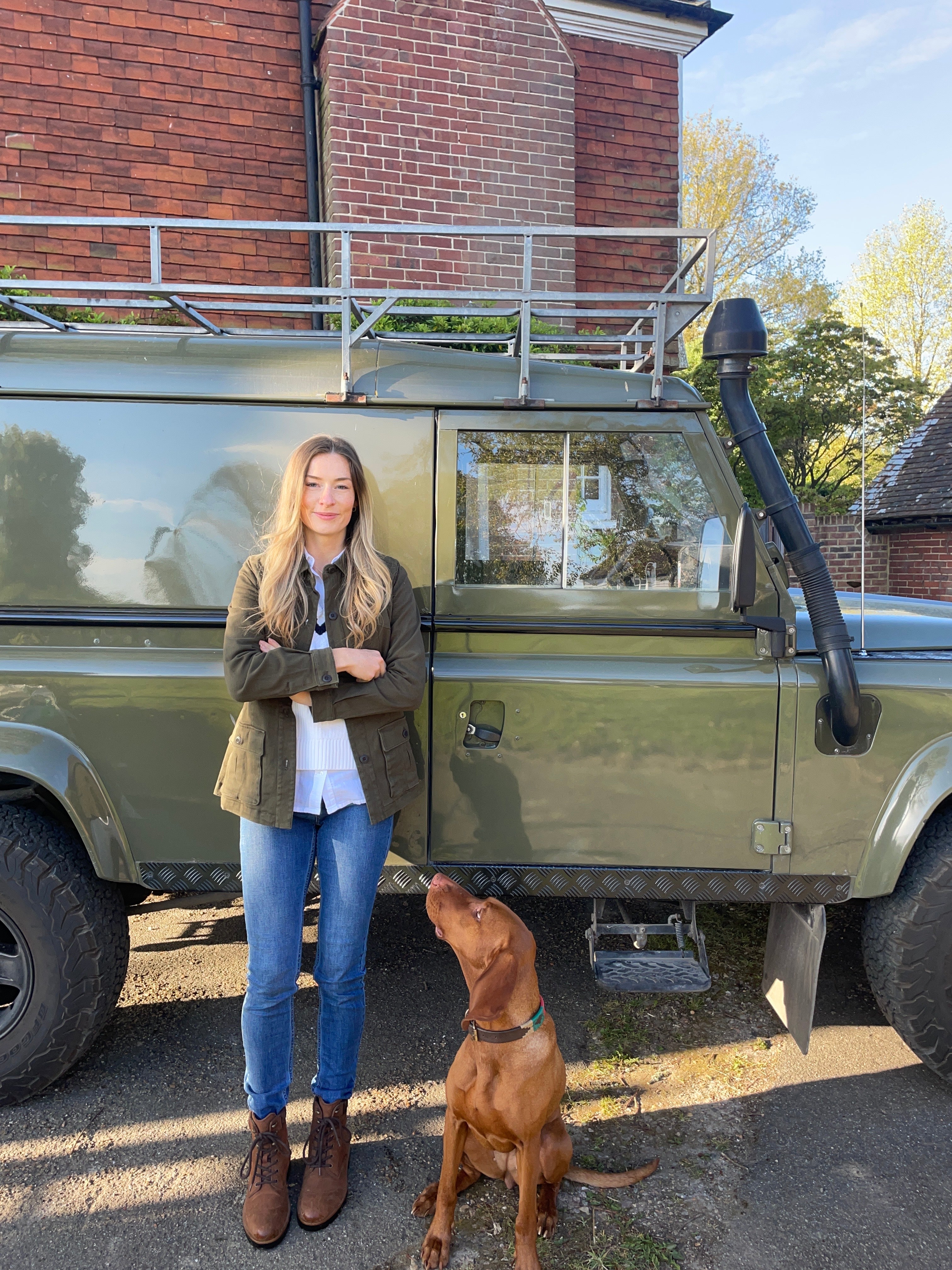 Two people standing next to a green vehicle with a dog on a driveway.