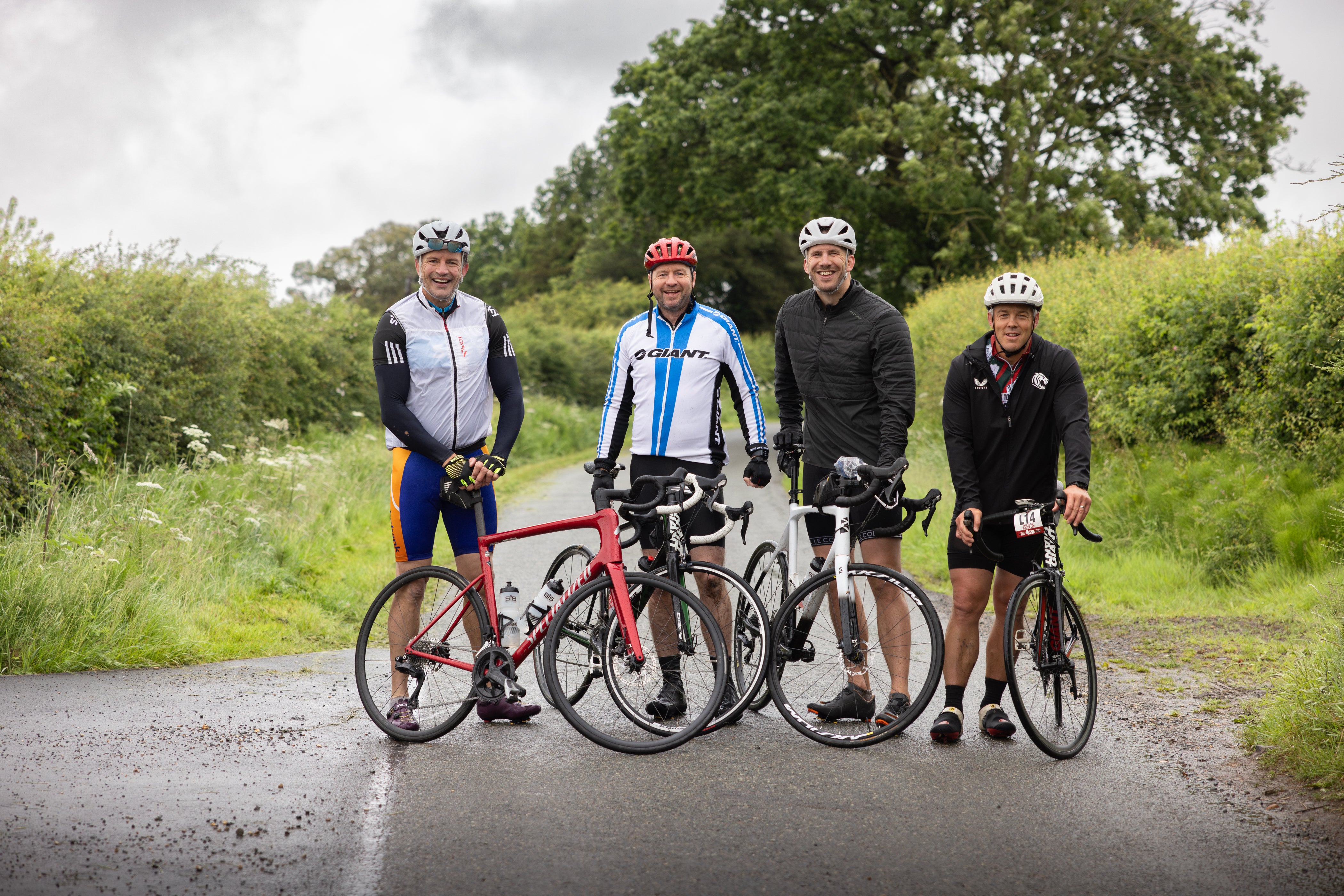 Four cyclists standing with their bicycles on a road surrounded by greenery