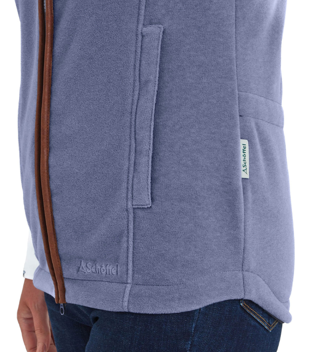 Close-up of the side panel of a stone blue fleece gilet, showing a vertical chest pocket and a hip-level hand-warmer pocket. A brown leather zip edge runs along the front opening, with a small Schöffel logo tab visible on the hem.