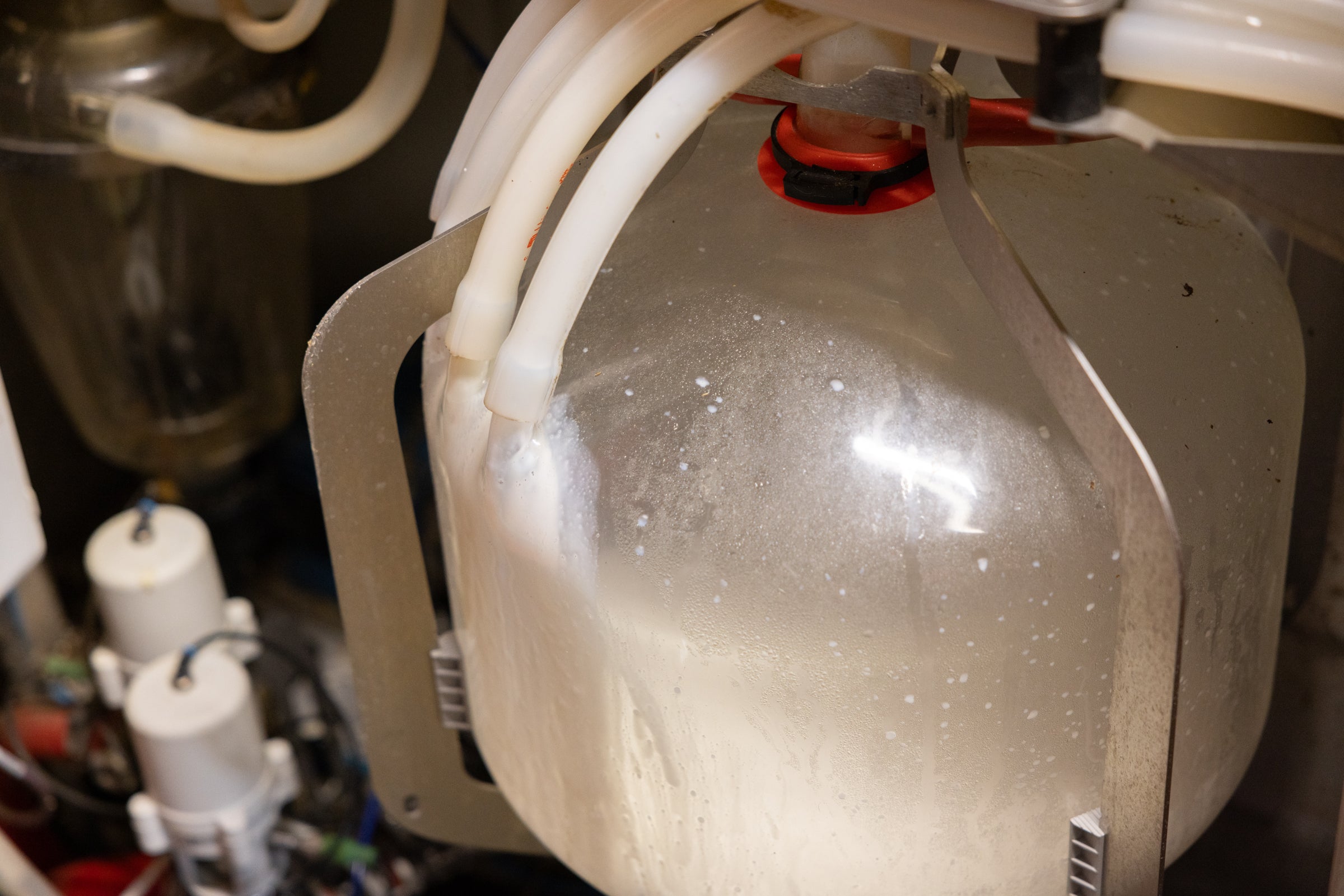 Close-up of a mechanical device with a transparent container and white hoses.