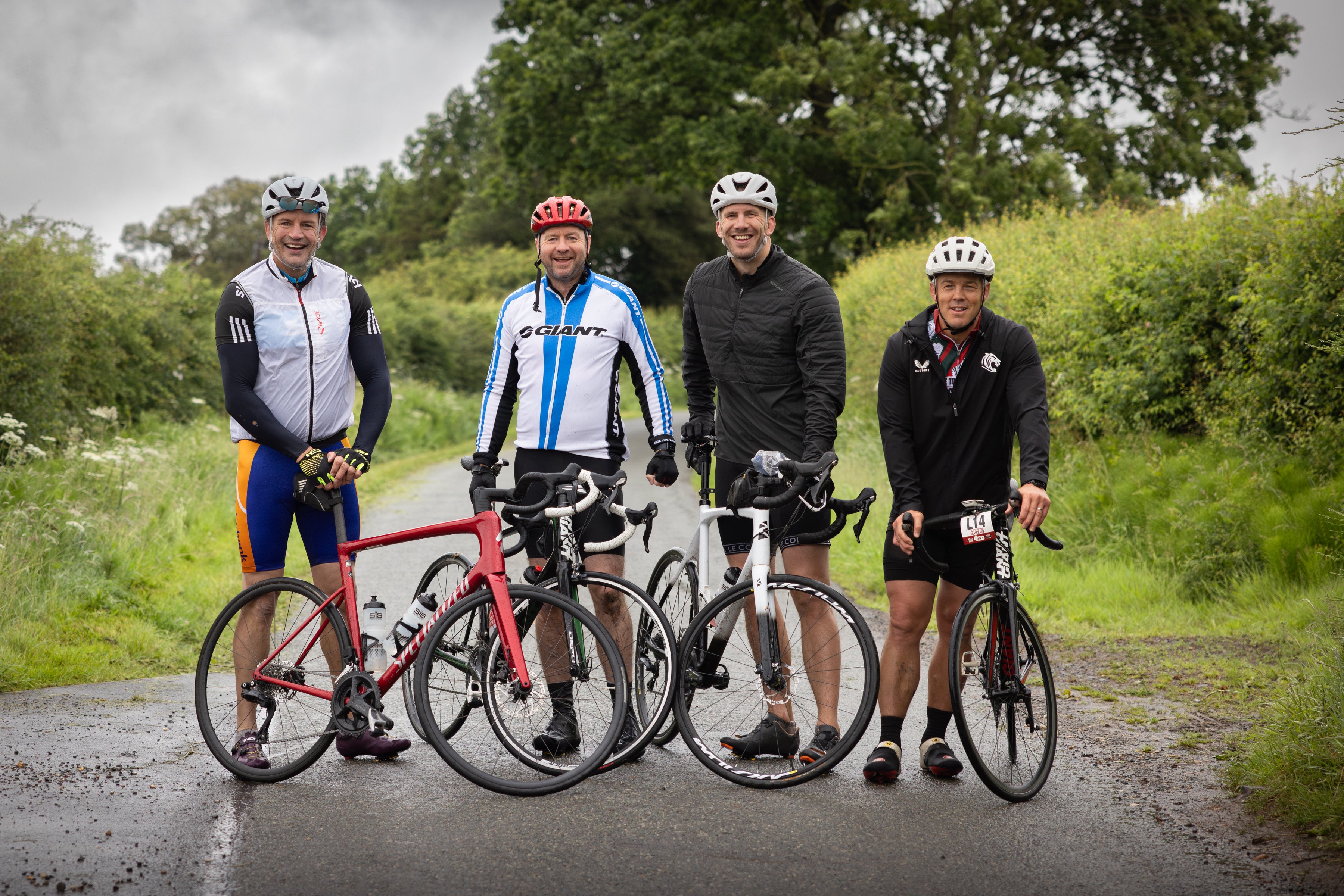 Four cyclists standing with their bicycles on a road surrounded by greenery