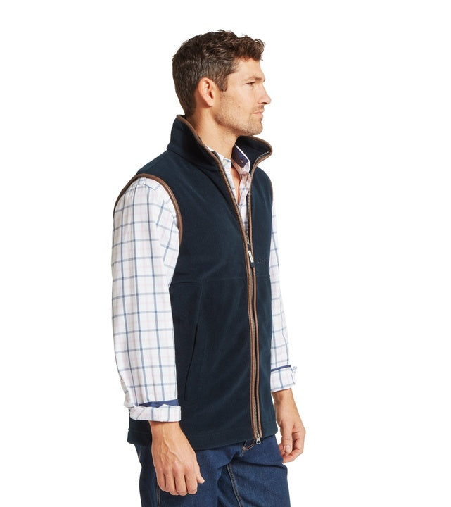 A side profile view of a man wearing a petrol blue fleece gilet with tan leather-trim full-length zip, worn over a white and blue checked shirt with jeans.