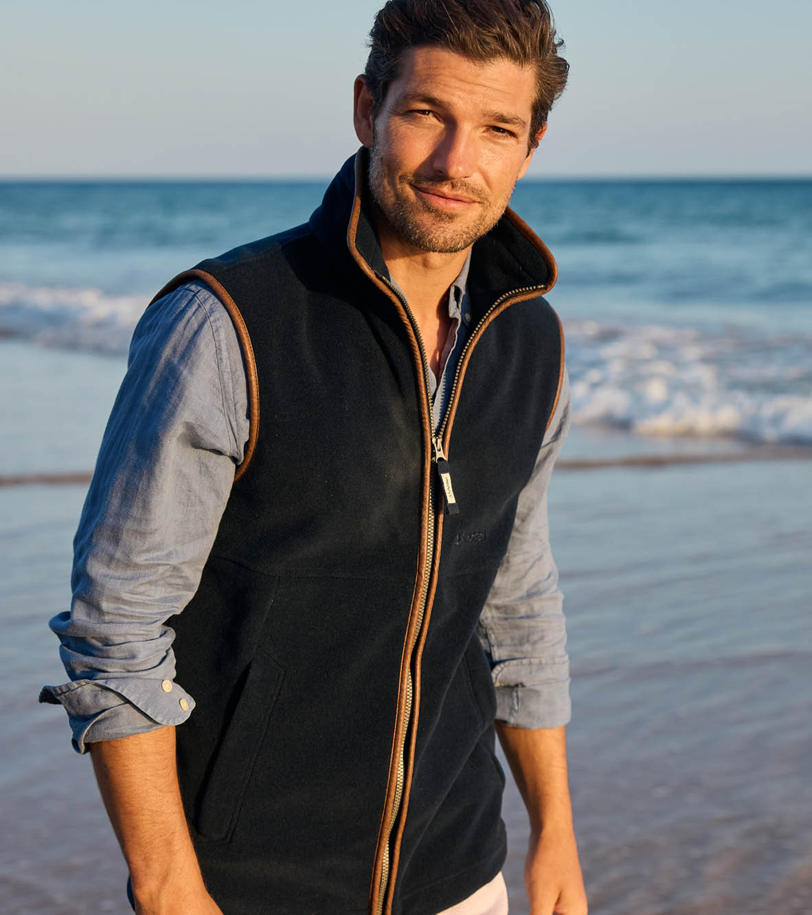 Man wearing a blue fleece gilet and a blue shirt on a beach