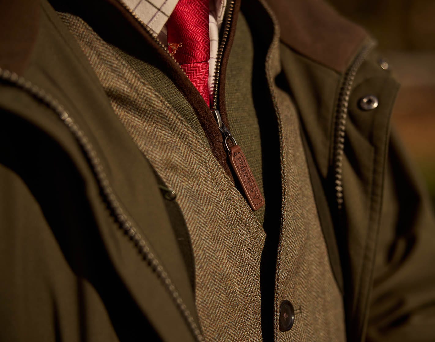Close-up of a person wearing a green jacket with a shirt underneath, blurred background