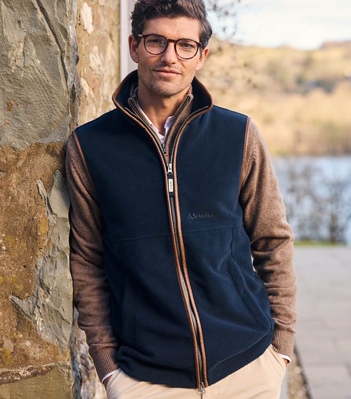 Man wearing a navy fleece gilet by a stone wall with a scenic background.