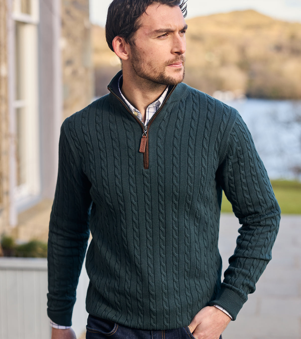 Man wearing a green cable knit sweater with a blurred outdoor background