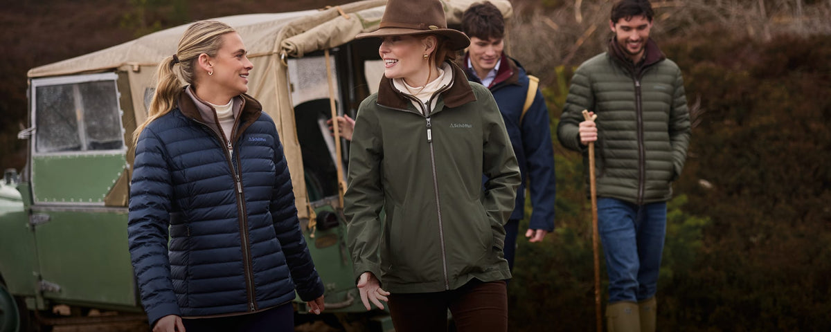 Four people outdoors in front of a vintage green canvas vehicle, wearing heavy insulated jackets.