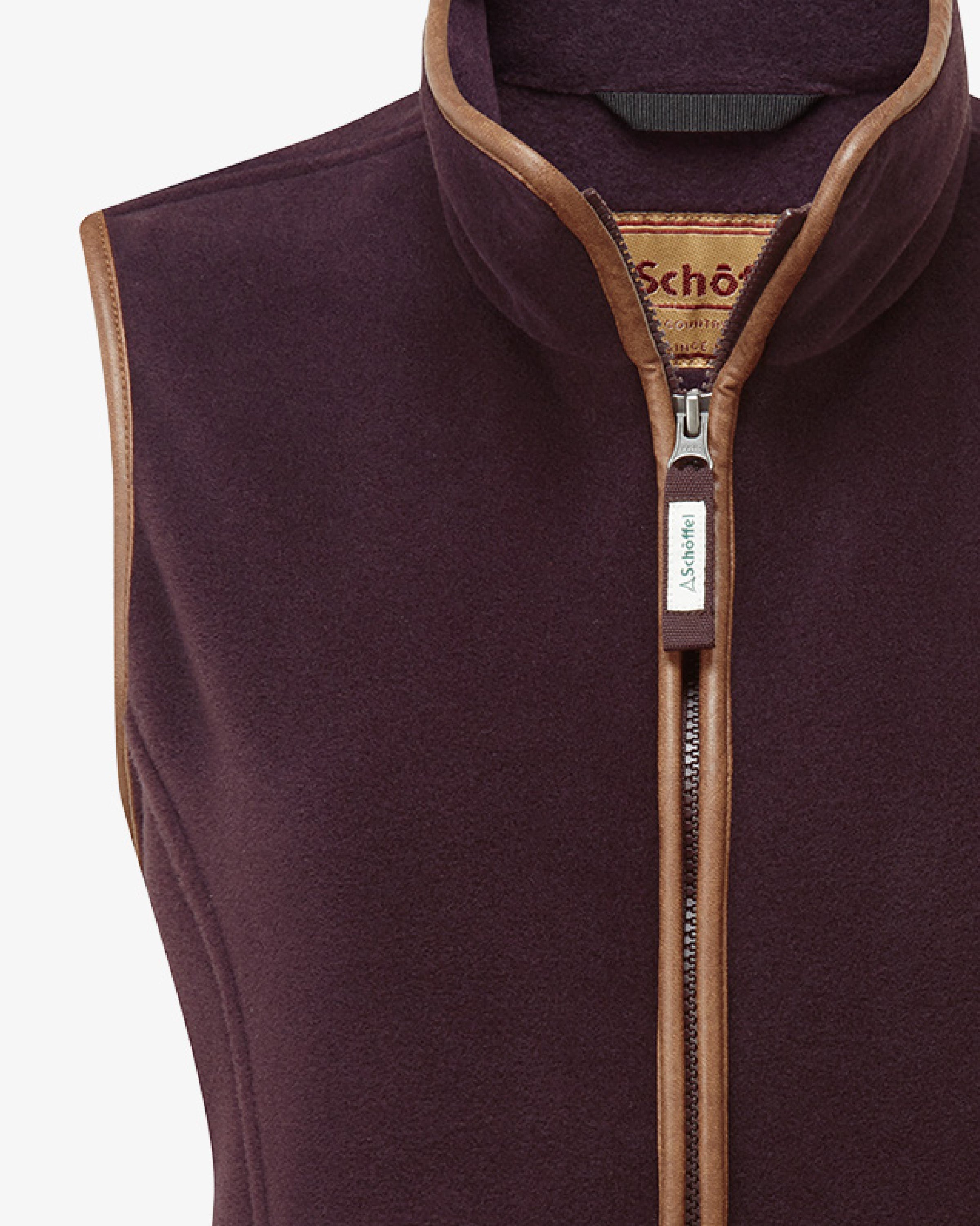 A close up of a dark plum coloured gilet with contrasting trim. Image highlights the full zip and the Schöffel embroidered logo.