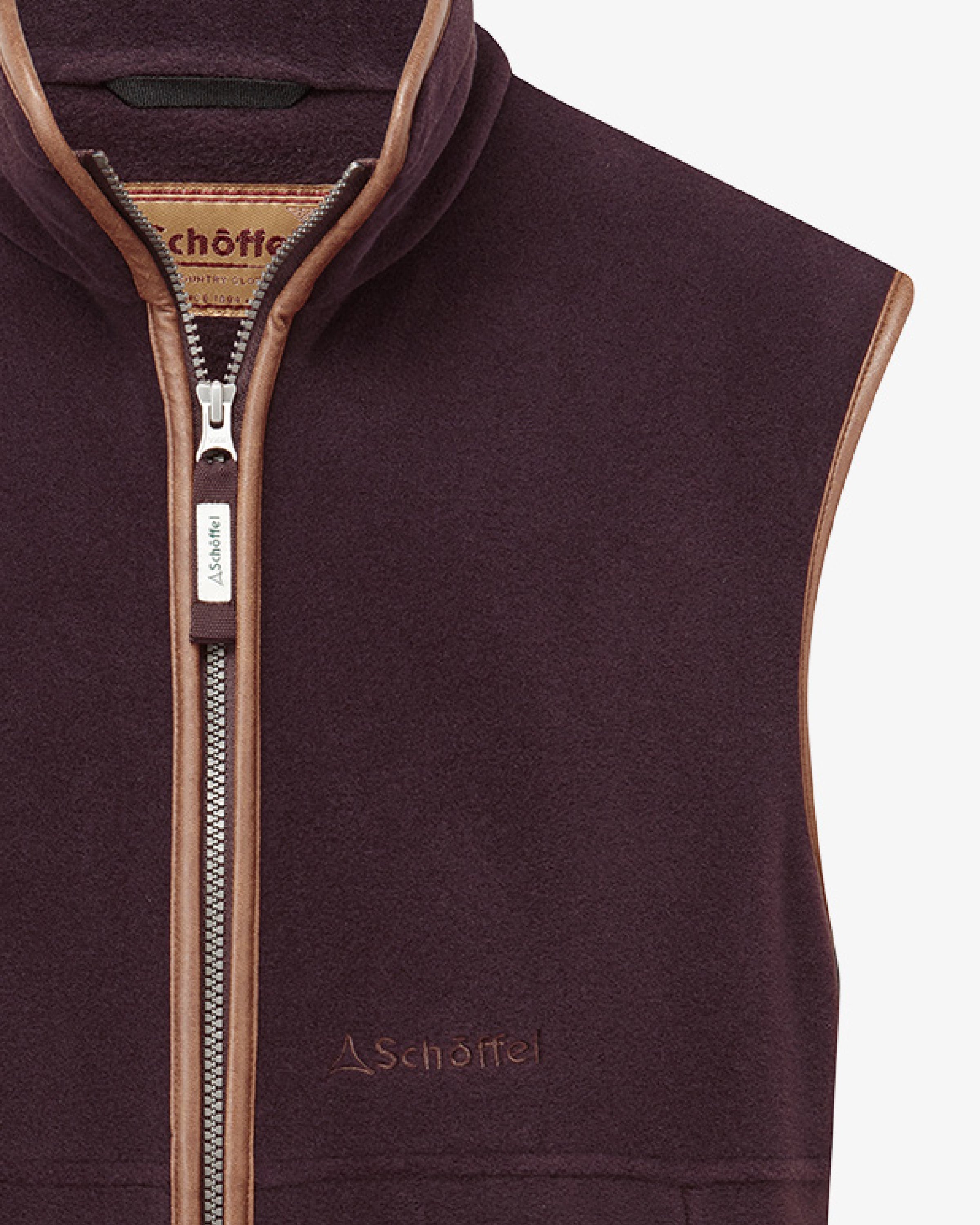 A close up of a dark plum coloured gilet with contrasting trim. Image highlights the full zip and the Schöffel embroidered logo.