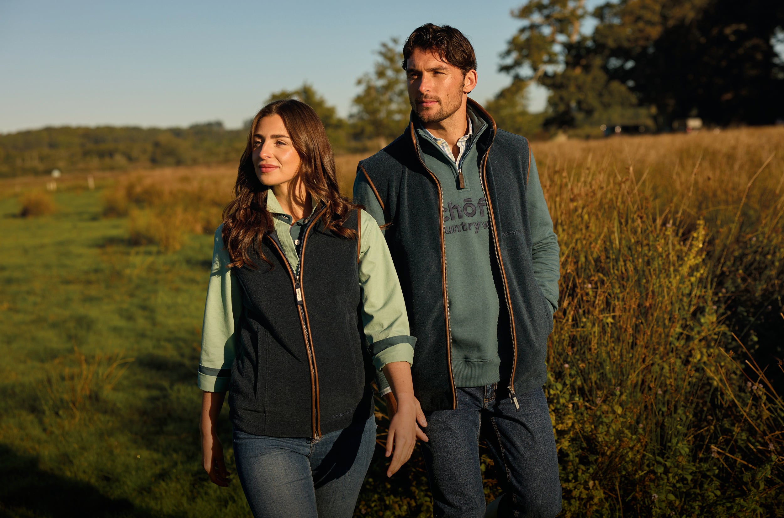 Two people walking in a field wearing matching jackets with visible branding.