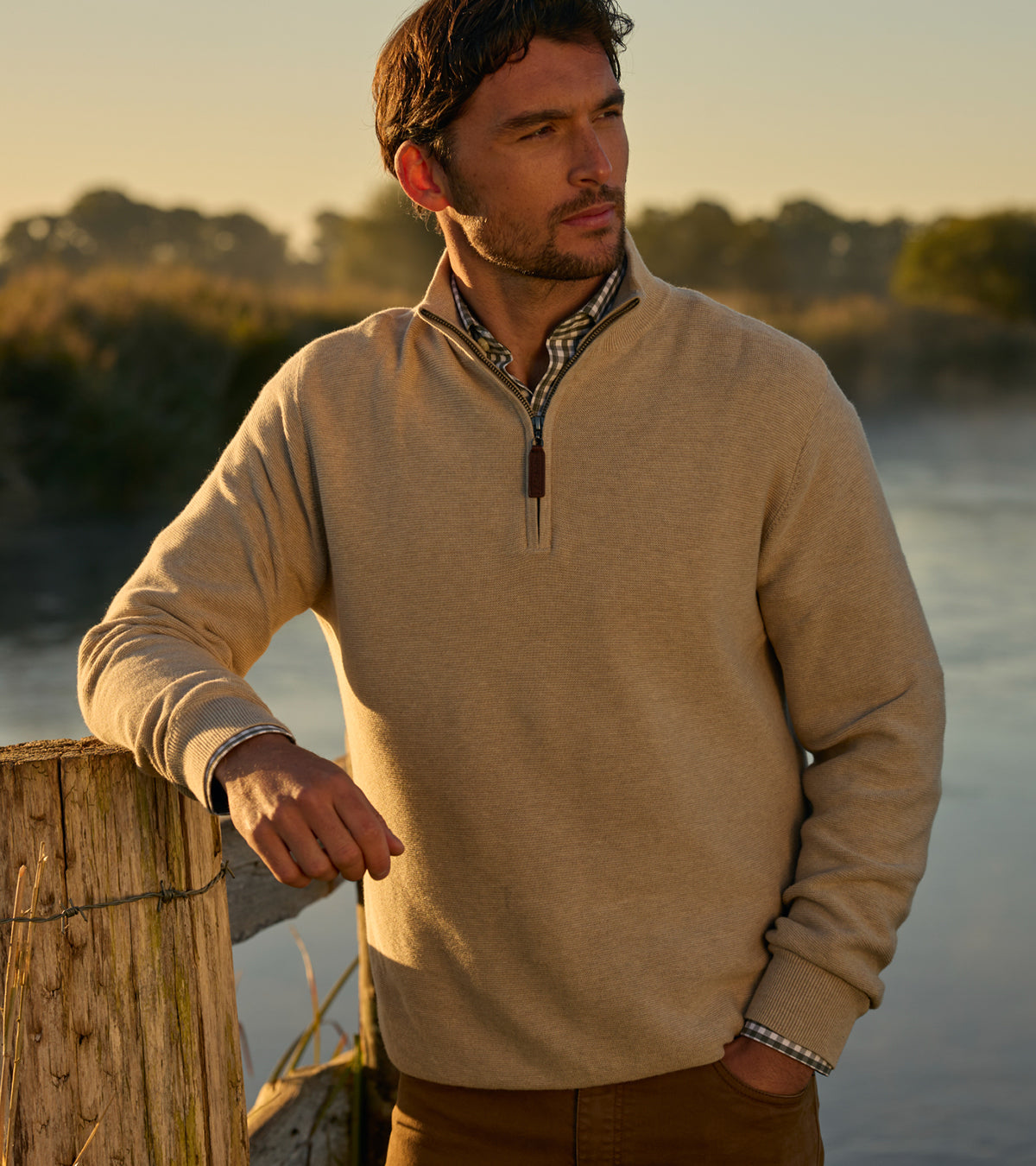 Man wearing a beige sweater by a body of water during sunset