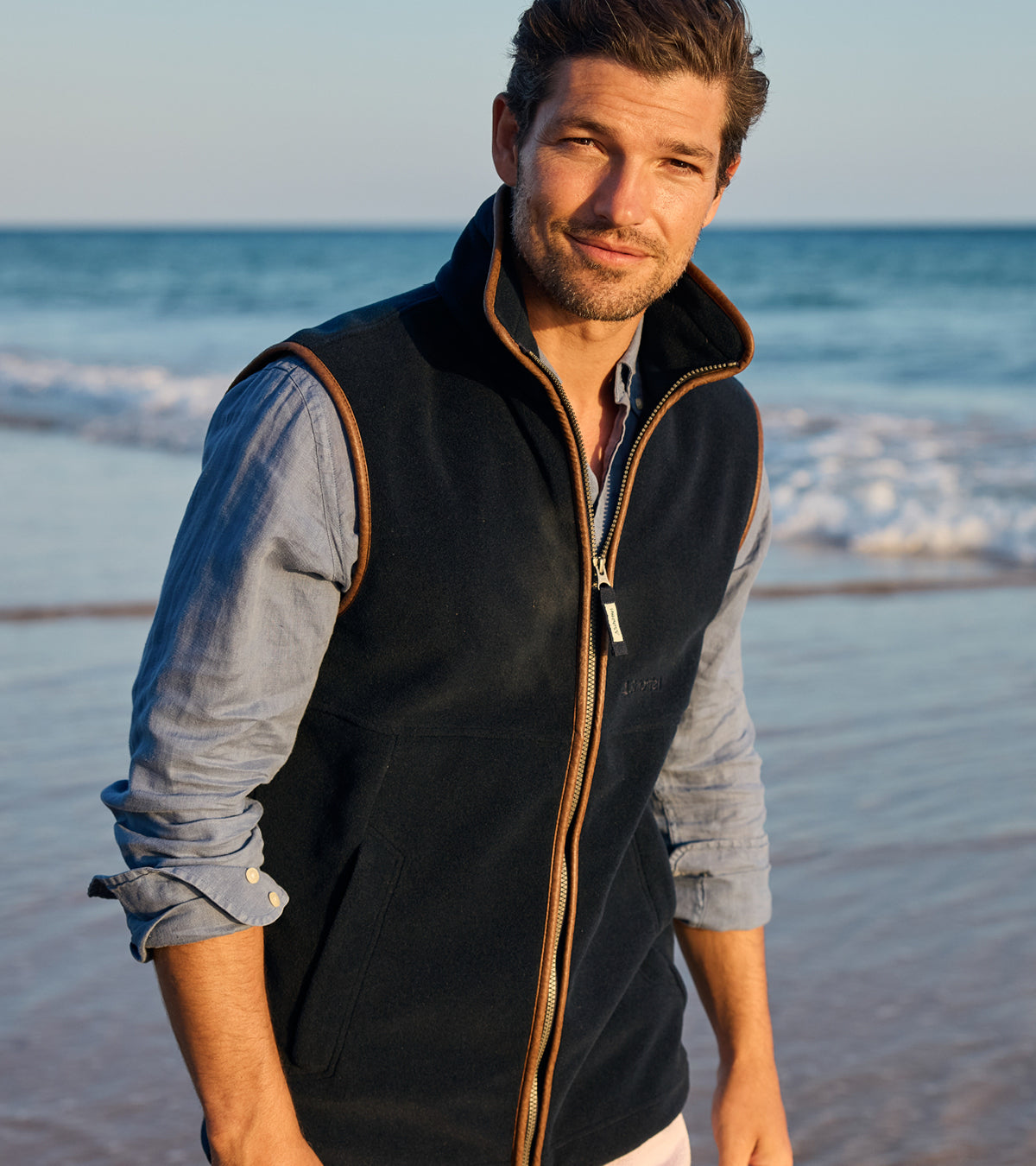 Man wearing a navy blue gilet over a blue shirt on a beach