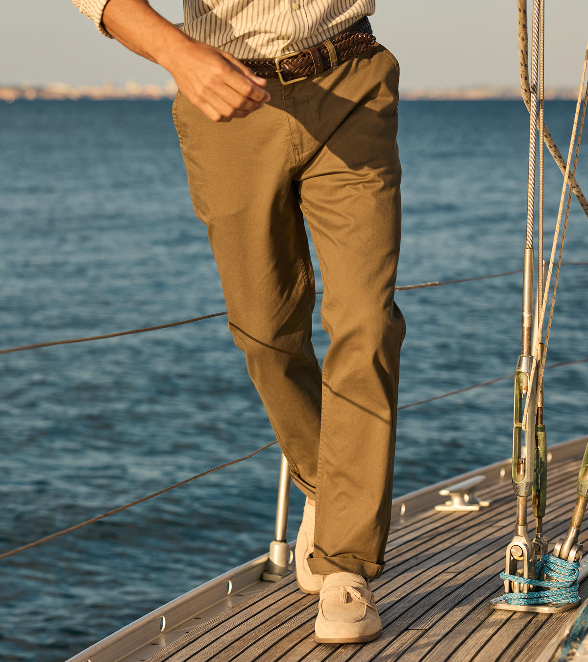 Person wearing brown pants standing on a boat deck with water in the background
