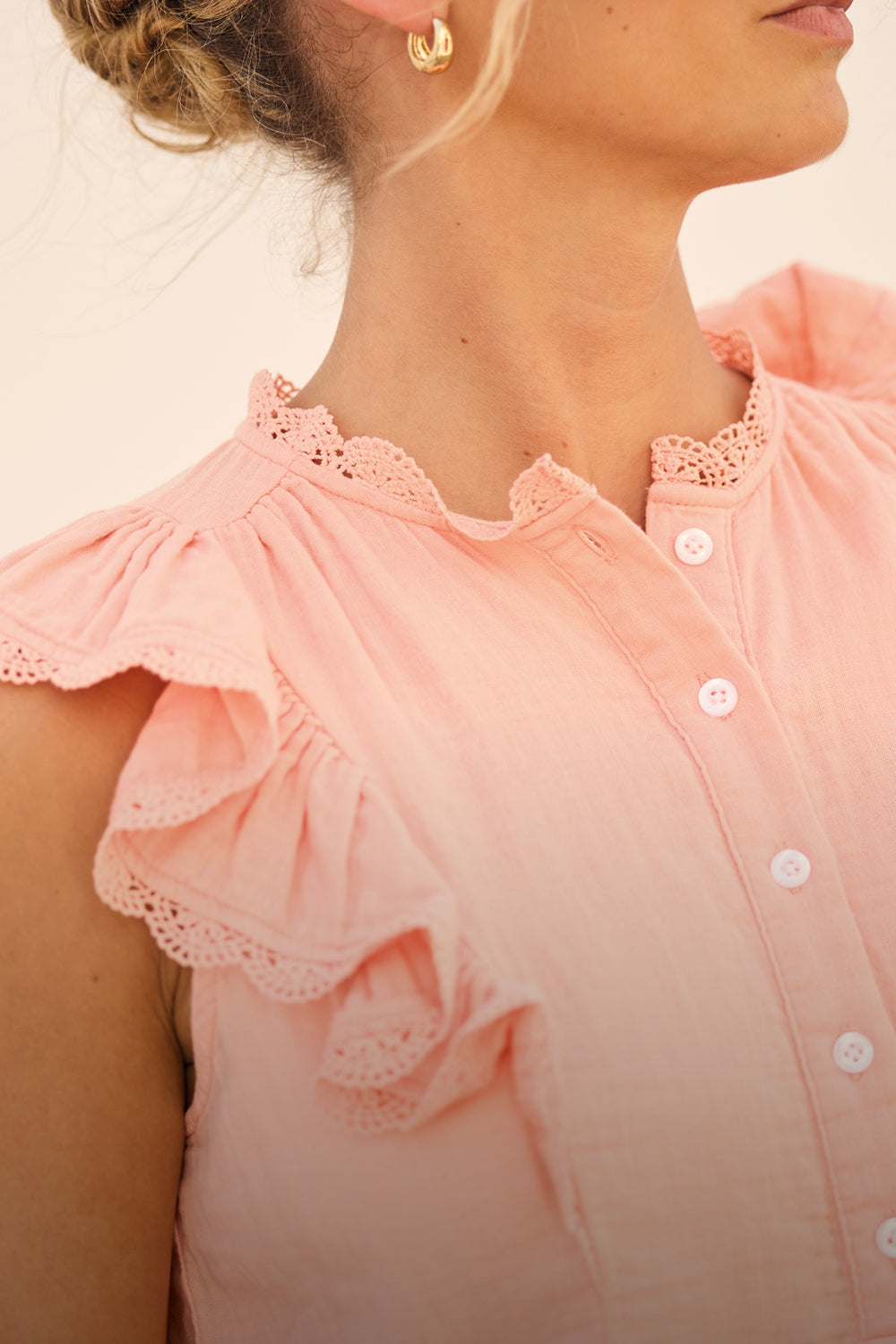 Close-up of a person wearing a pink blouse with lace details.