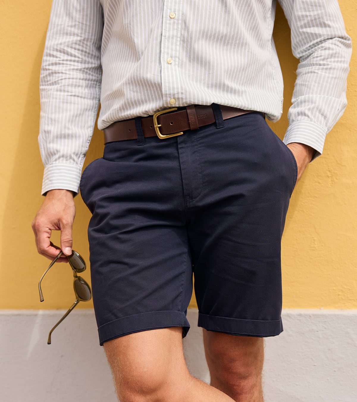 Person wearing navy shorts and a white shirt with a yellow background