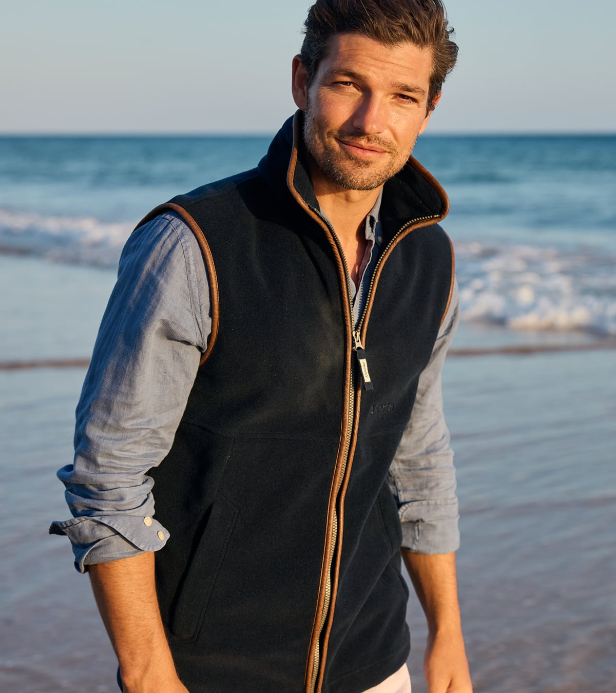 Man wearing a navy blue Schoffel gilet over a blue shirt on a beach